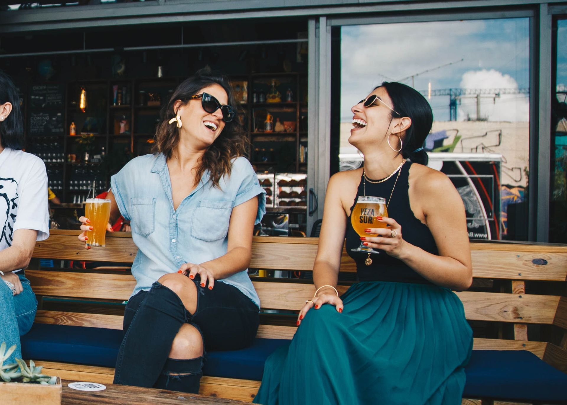 Two people laughing and drinking on a bench outside a café. Visit TwentyNine02 and explore flexible living options, including Townhomes in Universal City, TX.
