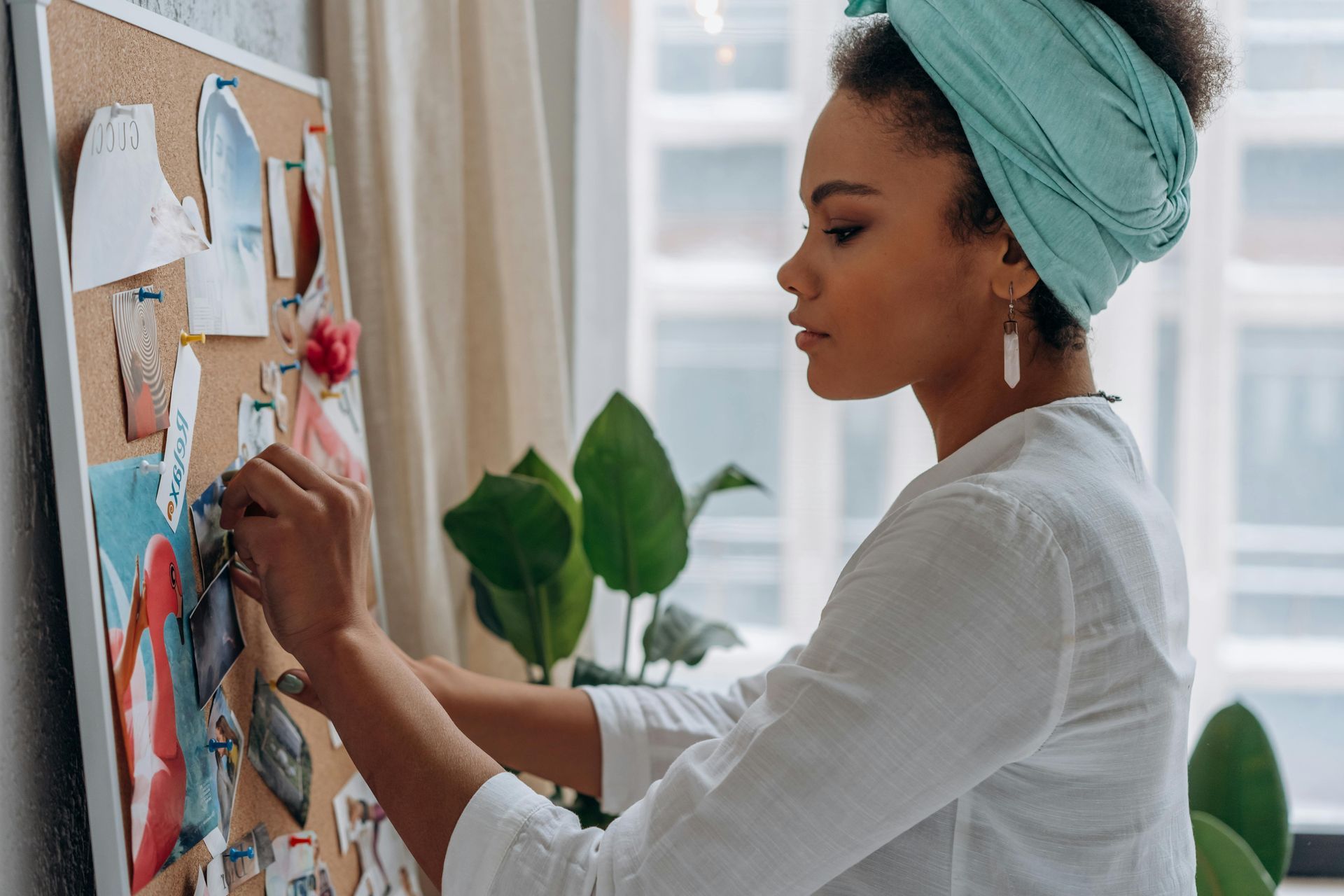 Woman pinning notes on a corkboard beside a window, with plants in the background. Schedule a walkthrough of TwentyNine02 and explore spacious One-Bedroom Apartments in Universal City, TX.