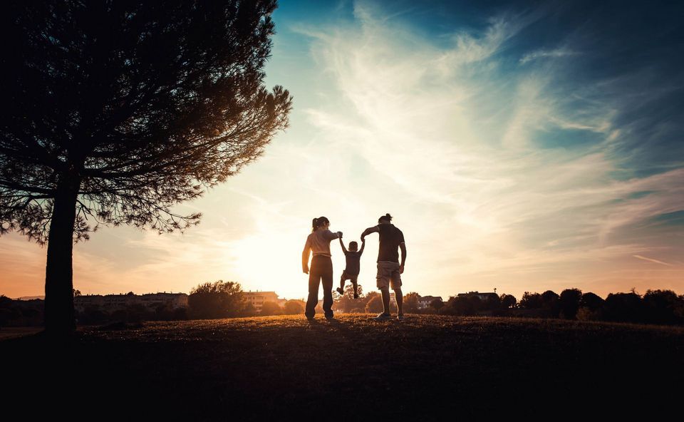 A family is standing in a park at sunset holding hands.