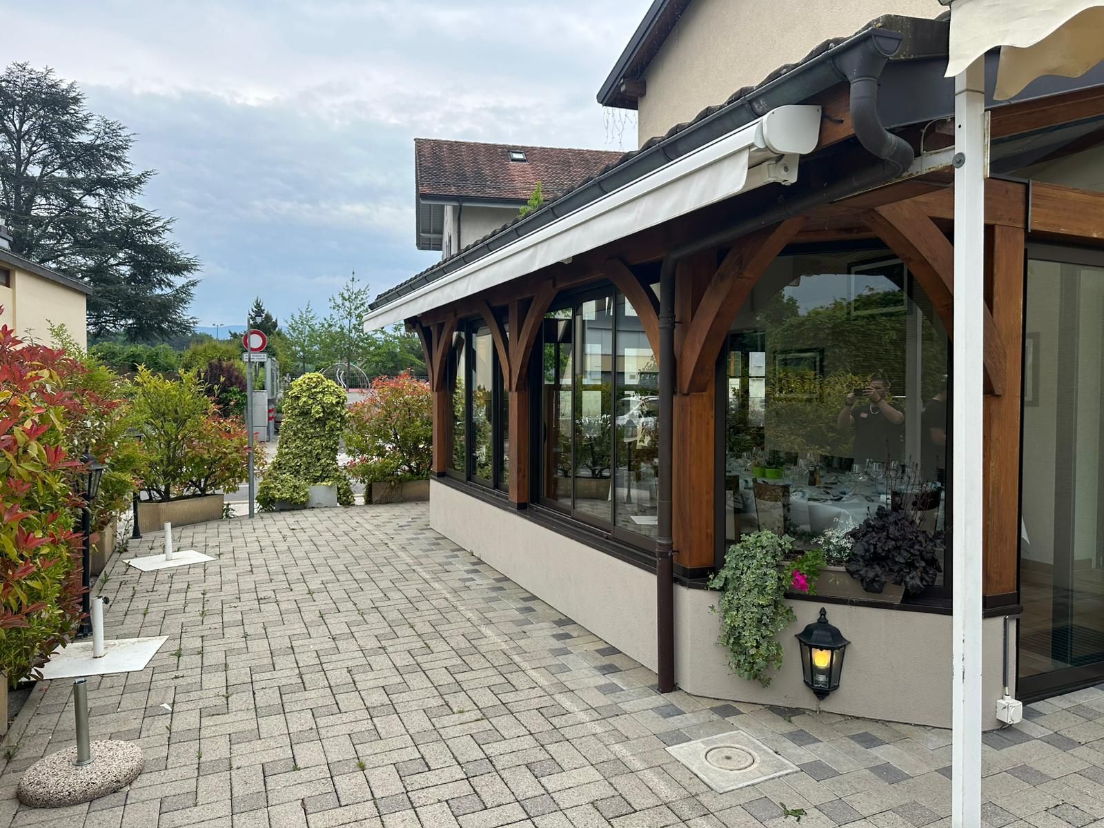 Extérieur d'un restaurant avec un auvent en bois, des tables et des plantes sur une terrasse en briques.