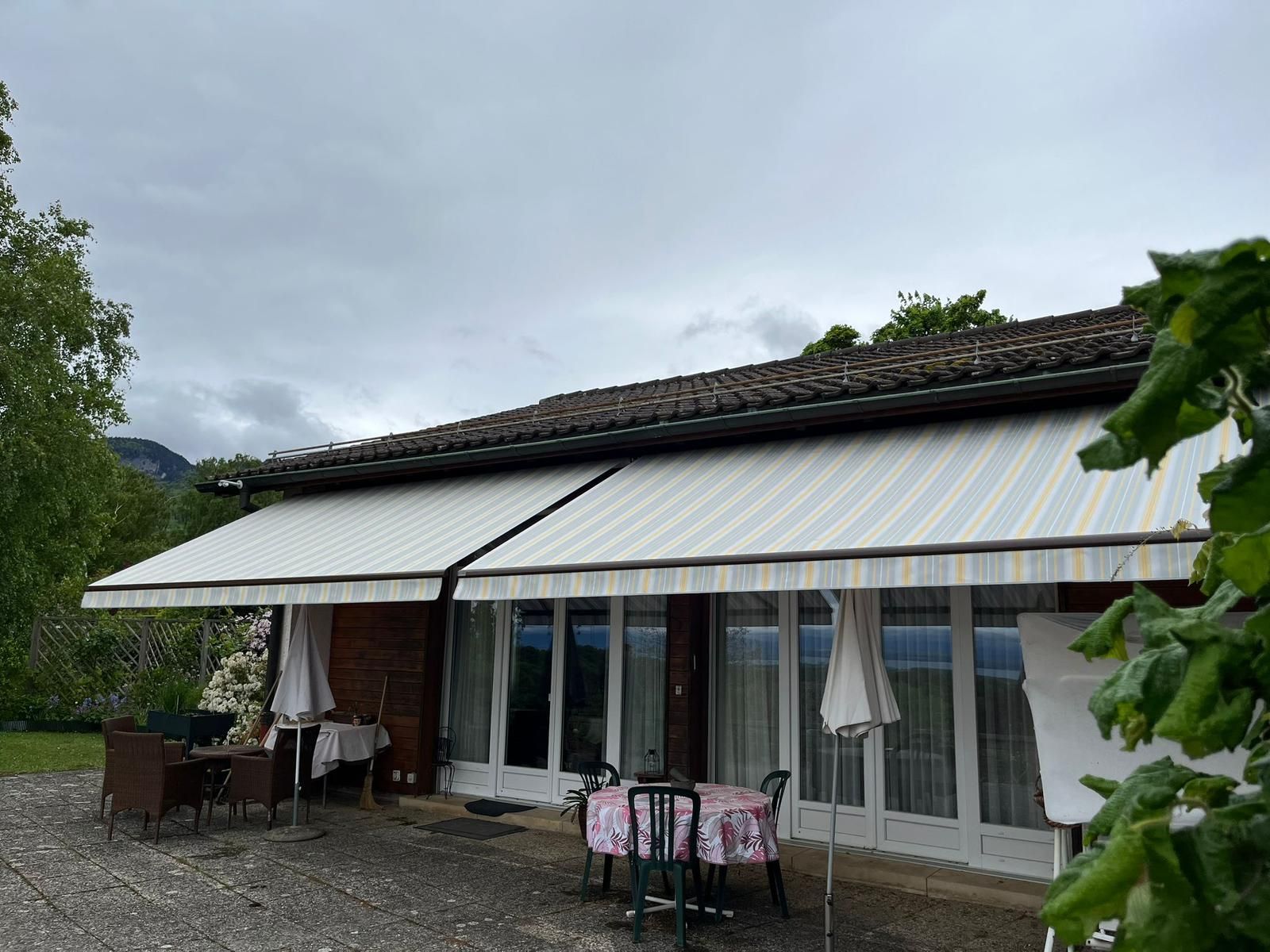 Une maison avec des auvents rayés, des sièges extérieurs sous un ciel nuageux.