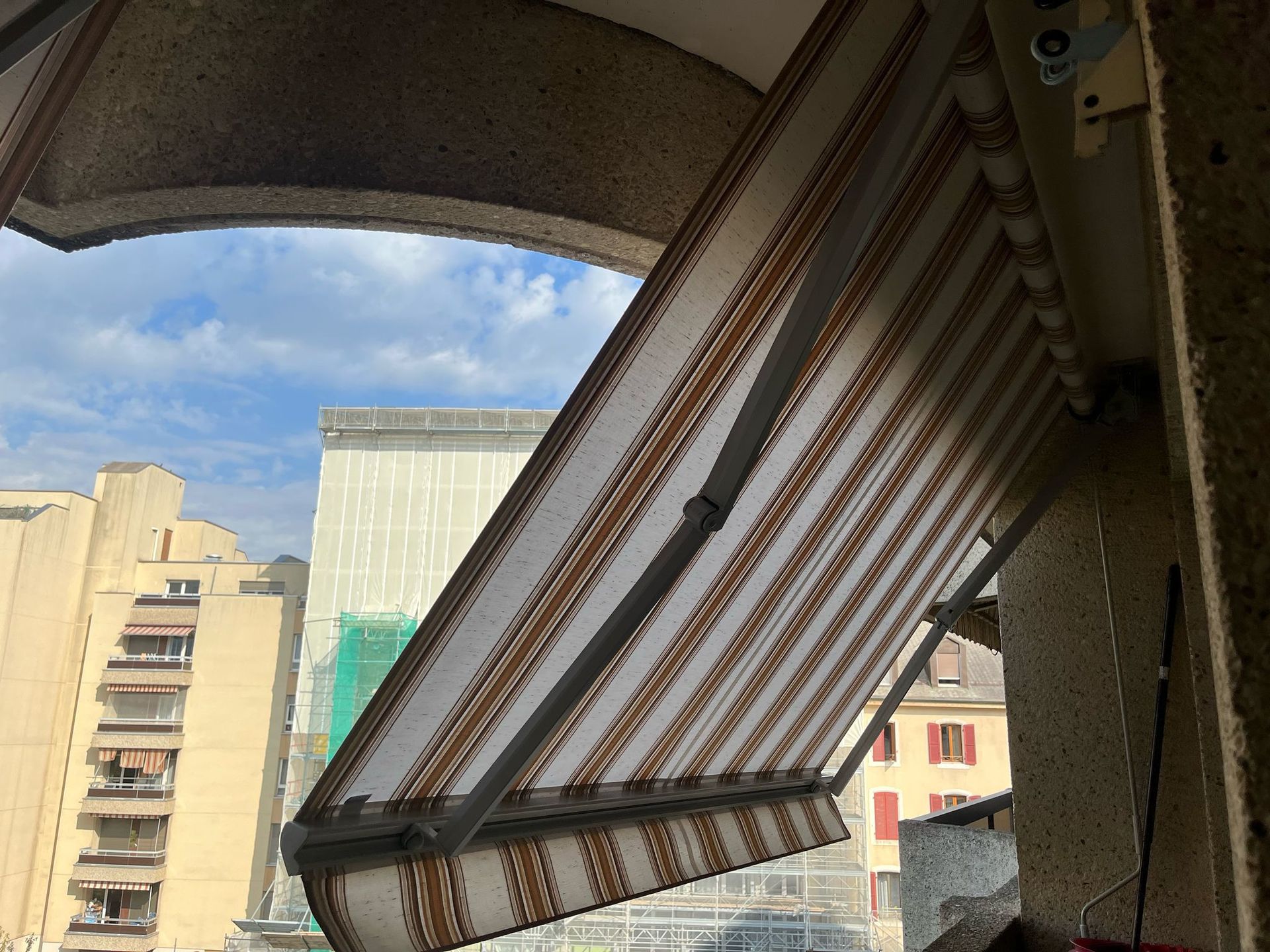 Auvents partiellement étendus sur un balcon donnant sur les bâtiments de la ville.