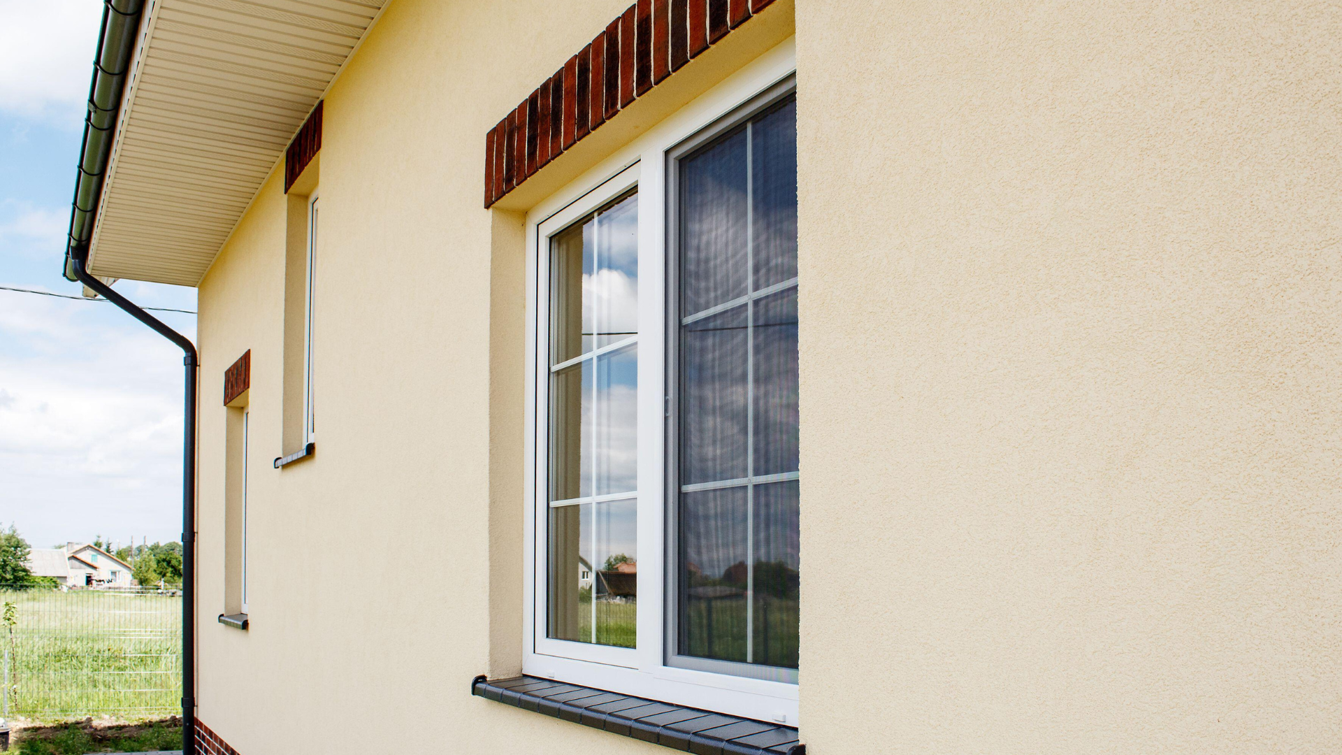 Extérieur de maison beige avec fenêtre blanche, accent de brique et gouttière.