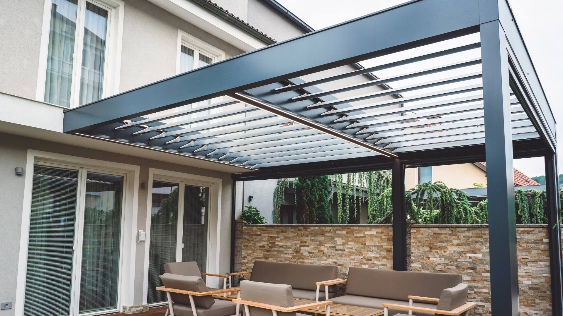 Pergola sur patio avec mobilier, rattachée à un bâtiment de couleur claire.