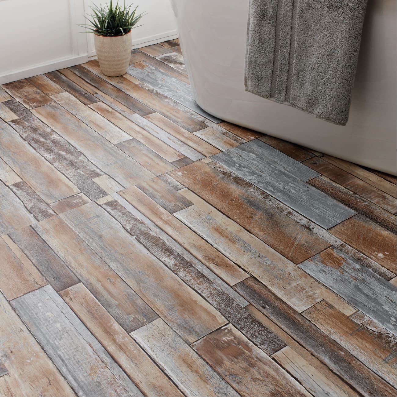 Rustic wood-plank flooring with weathered gray and brown tones, located in a bathroom next to a white bathtub.