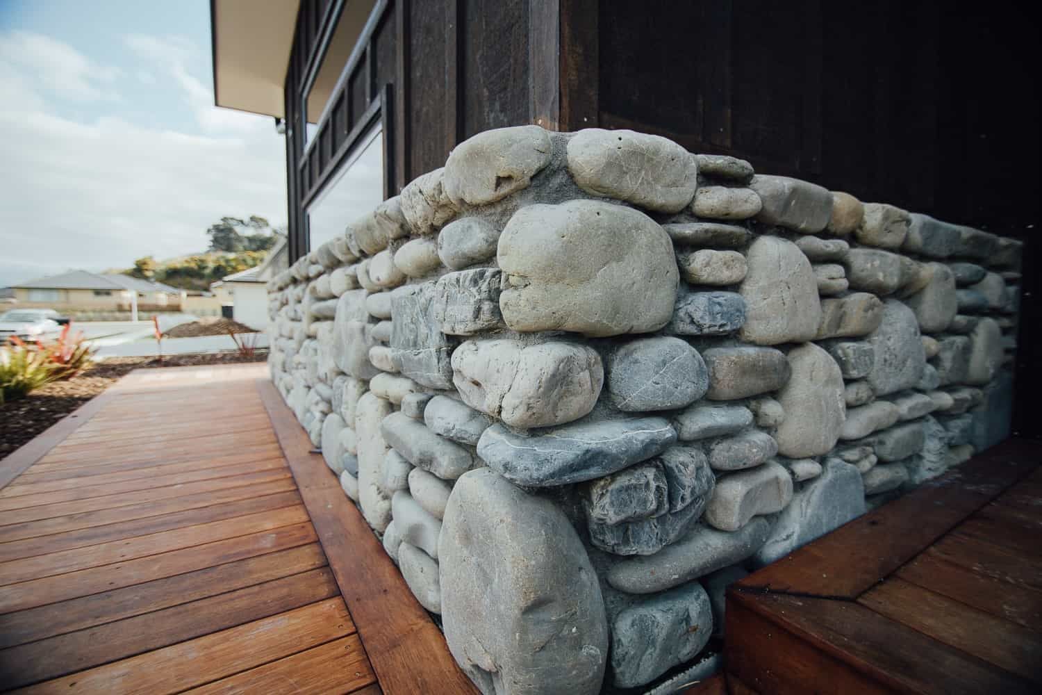 A low stone wall made of rounded, light-gray river rocks, bordering a wooden deck and a dark wooden building exterior.