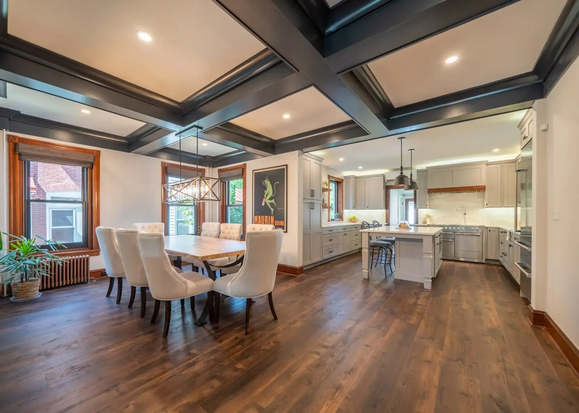 Open-concept kitchen and dining area with a coffered ceiling, hardwood floors, a dining table, and light-colored chairs.