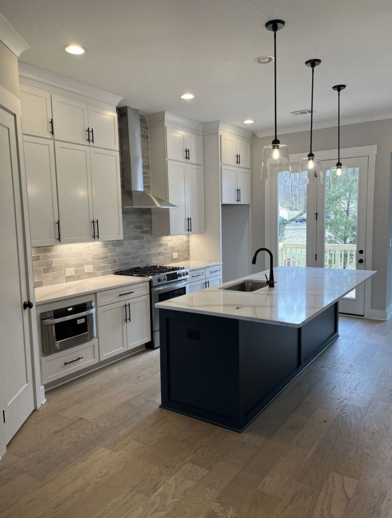 A modern kitchen with white upper cabinets, a dark blue island, quartz countertops, and three hanging pendant lights.