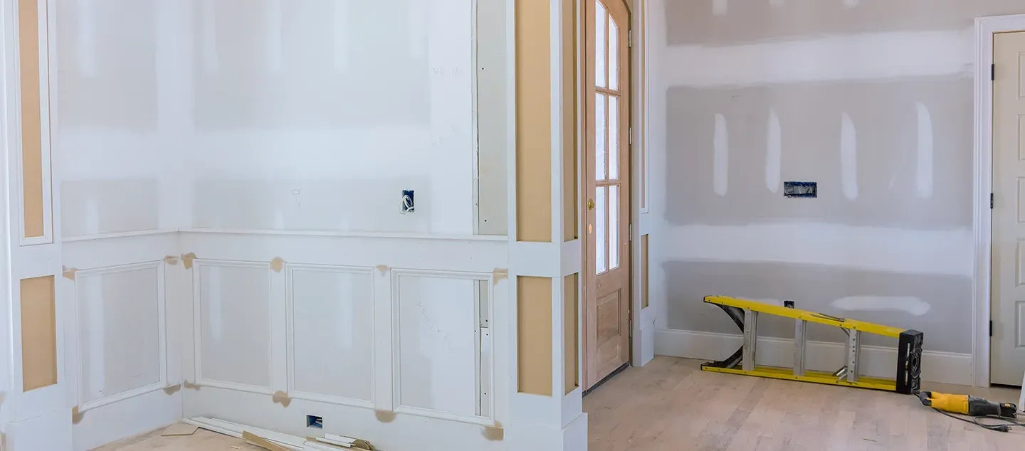 An interior room under construction with white drywall, wooden paneling, a wooden door, and a yellow work trestle.