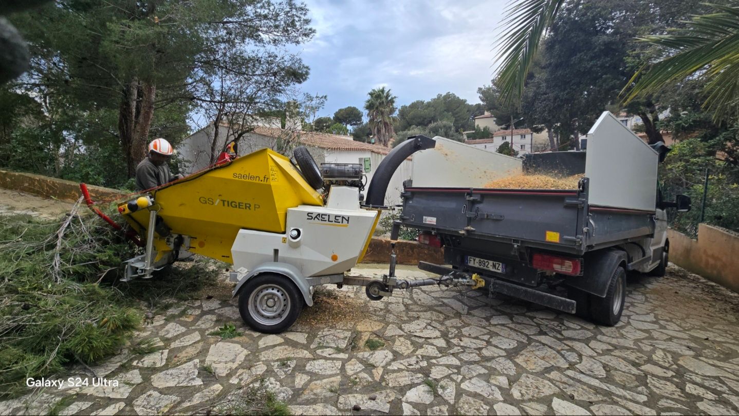 Un homme alimente un broyeur de branches, fixé à un camion. Broyage de bois en extérieur.