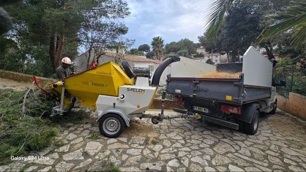 Un homme alimente un broyeur de branches, fixé à un camion. Broyage de bois en extérieur.