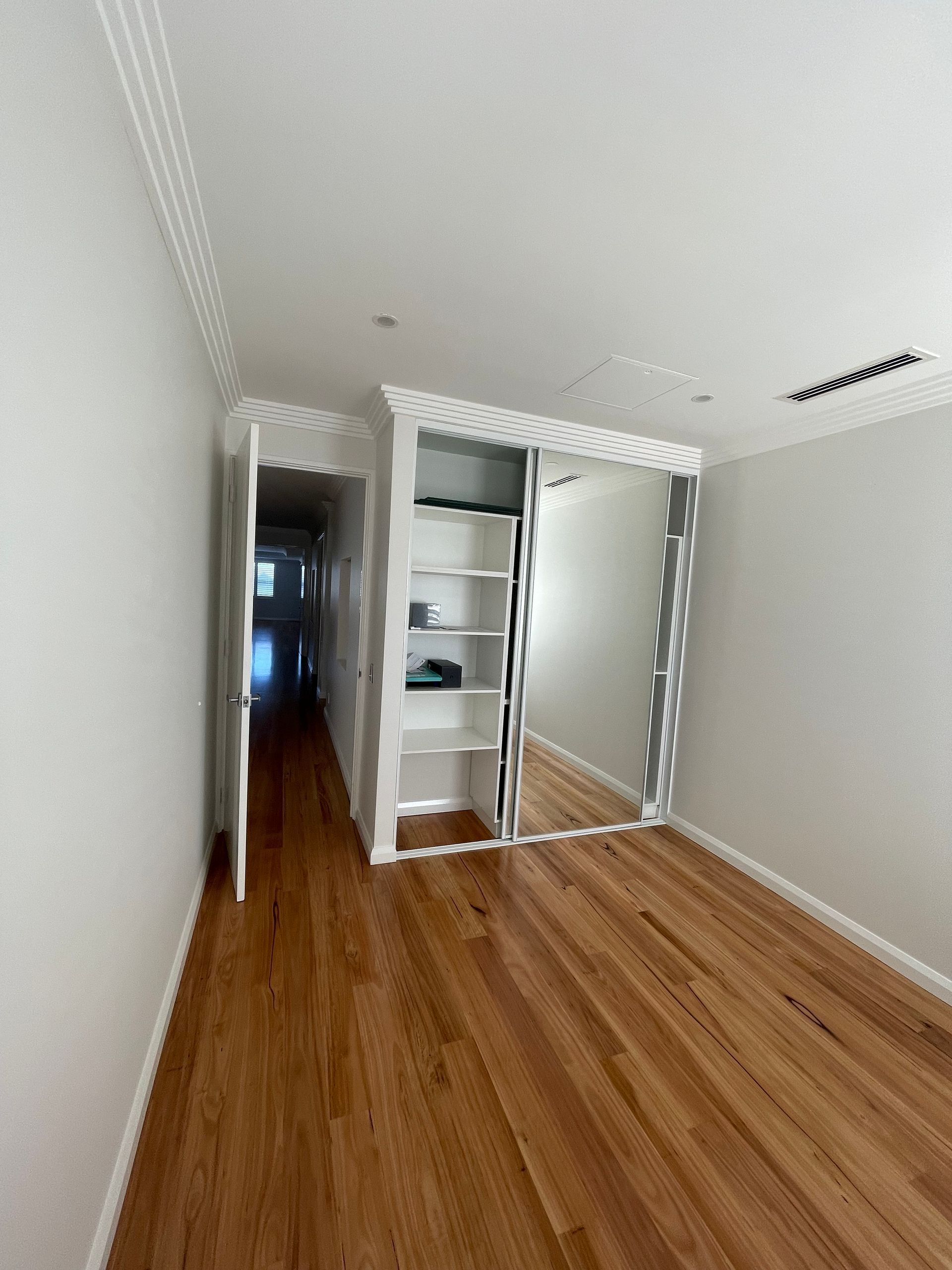 An empty room with hardwood floors and a large mirror.
