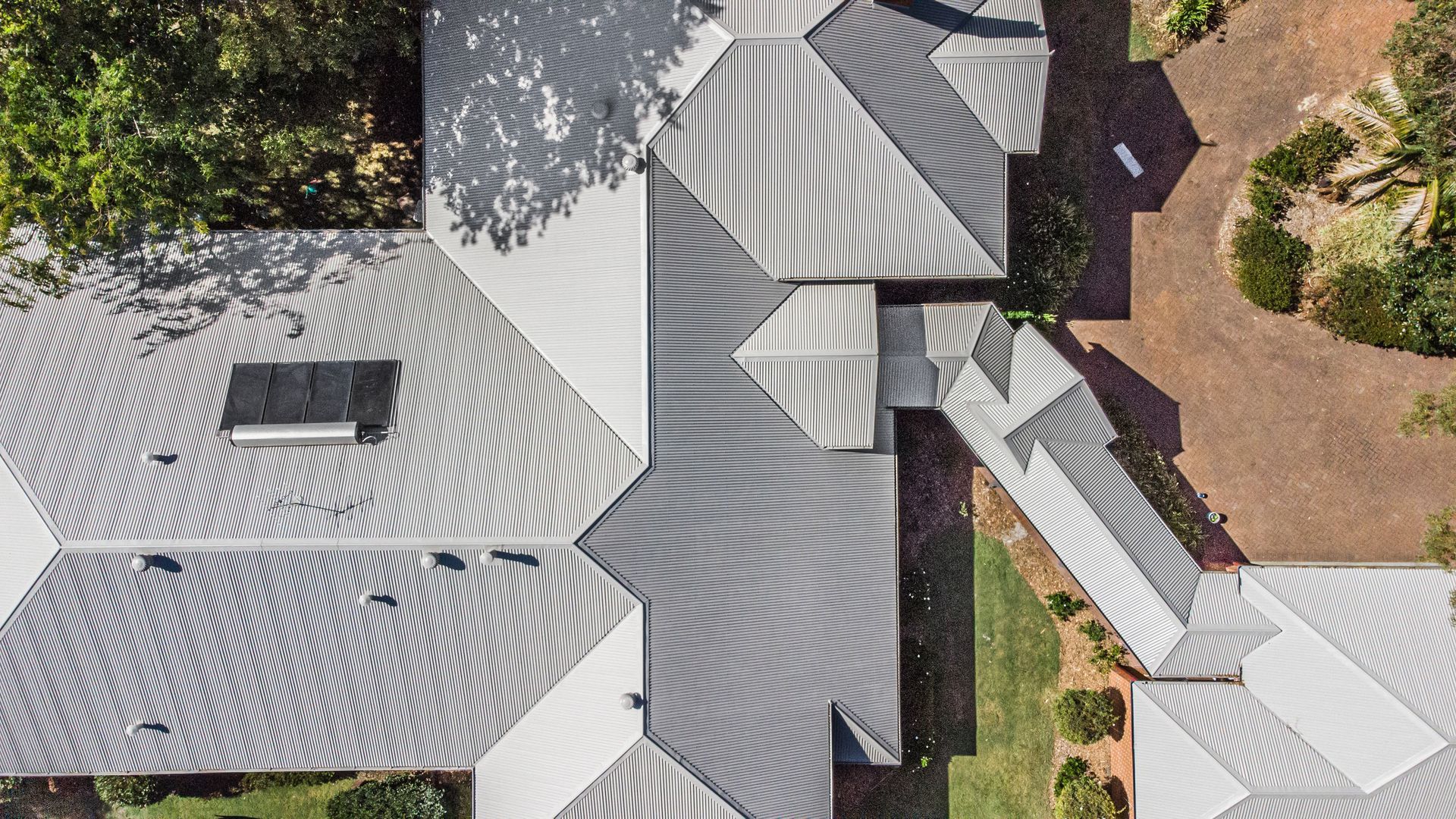 An aerial view of a large house with a gray roof surrounded by trees.