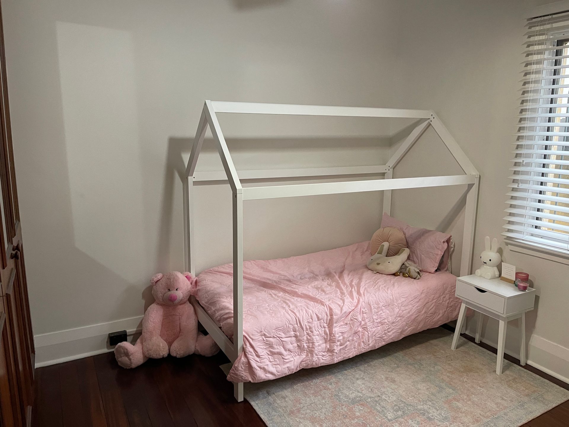A bedroom with a bed in the shape of a house and a teddy bear.