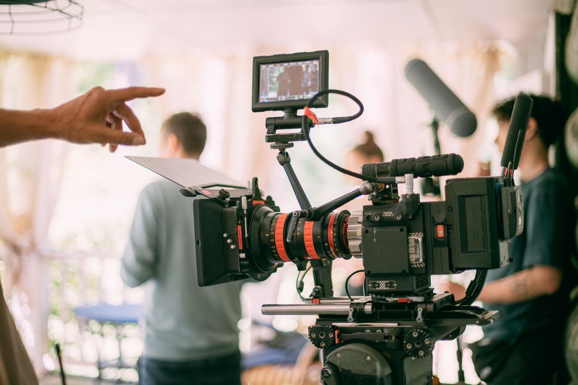 Film camera setup on a studio set, with crew members and a hand pointing toward the shot.