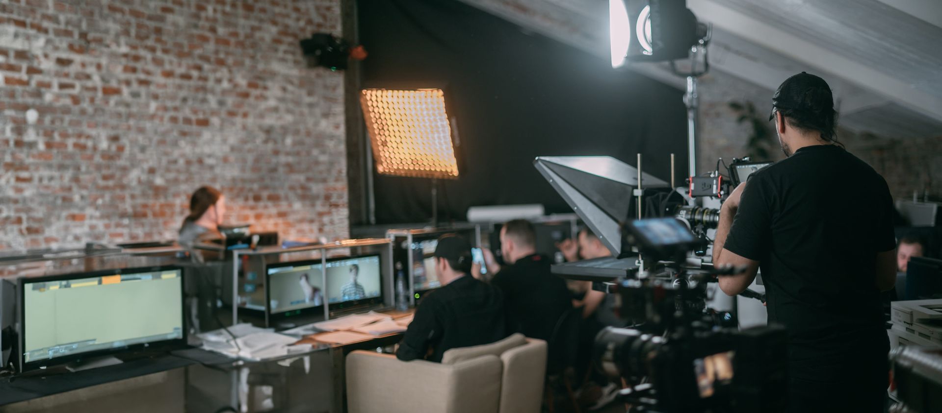 Film crew working in a studio with monitors, lights, and a brick wall backdrop
