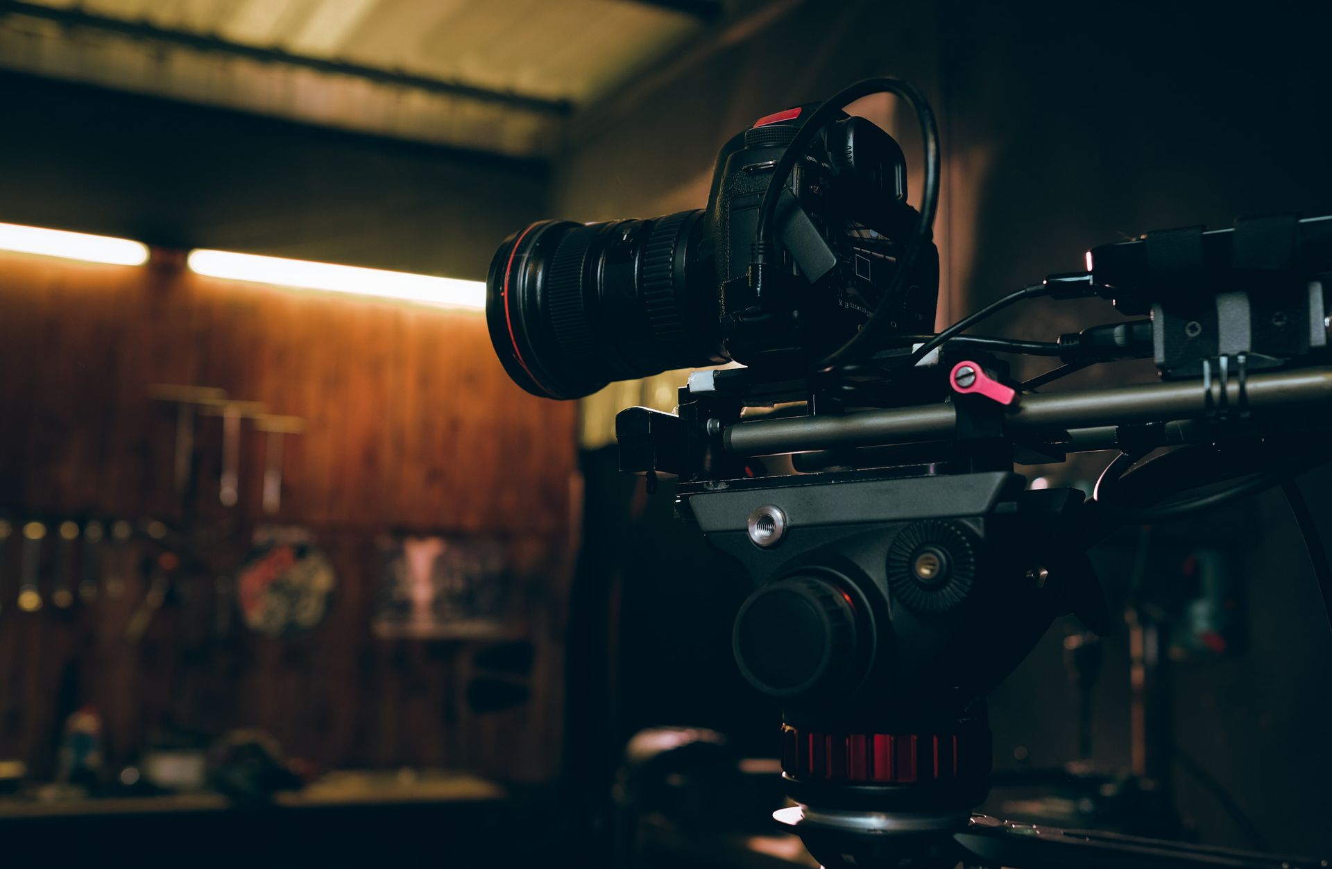 Camera on a tripod in a dimly lit room with warm wood paneling and a blurred background