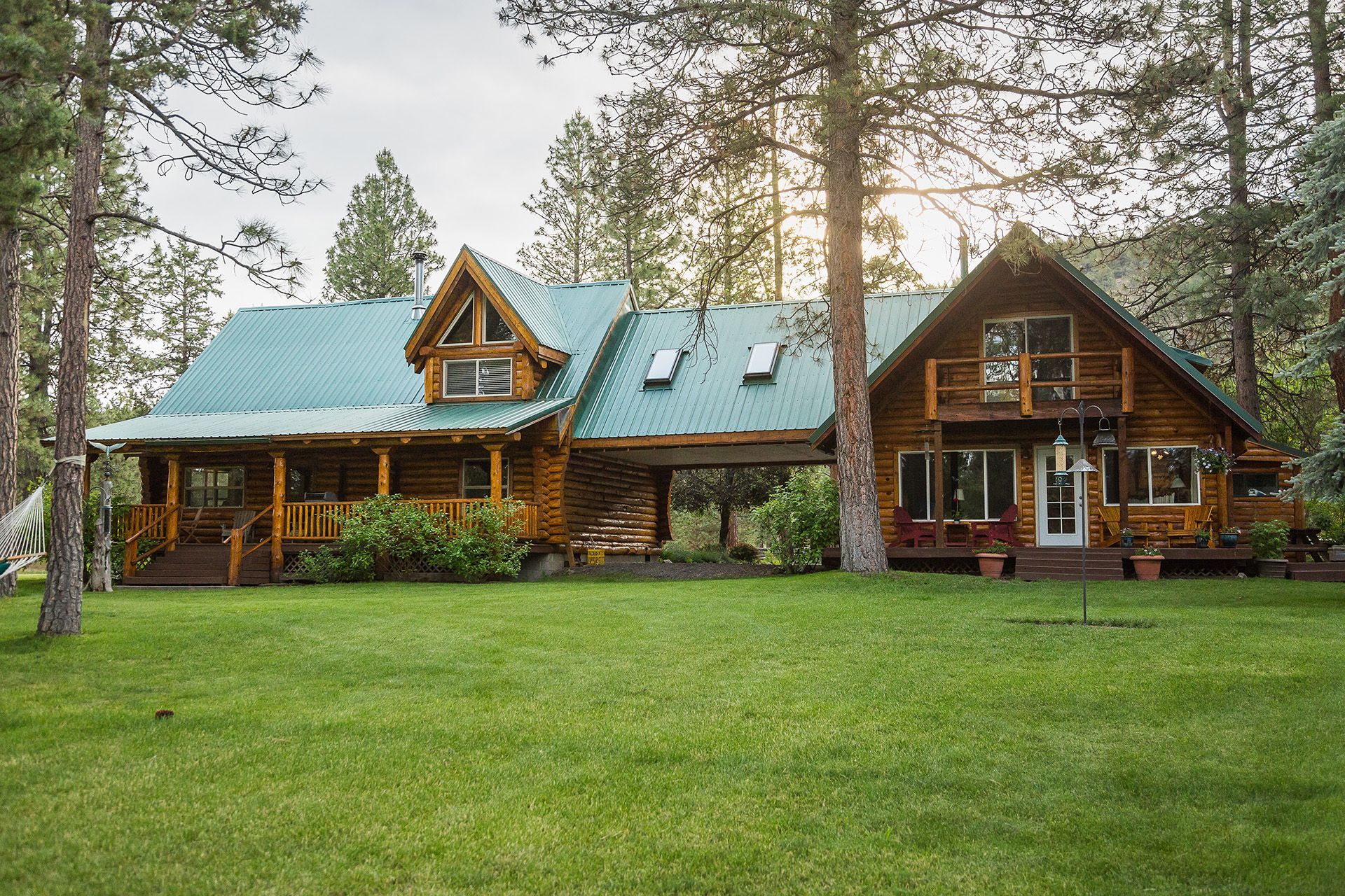 A large log cabin with a green roof is surrounded by trees.