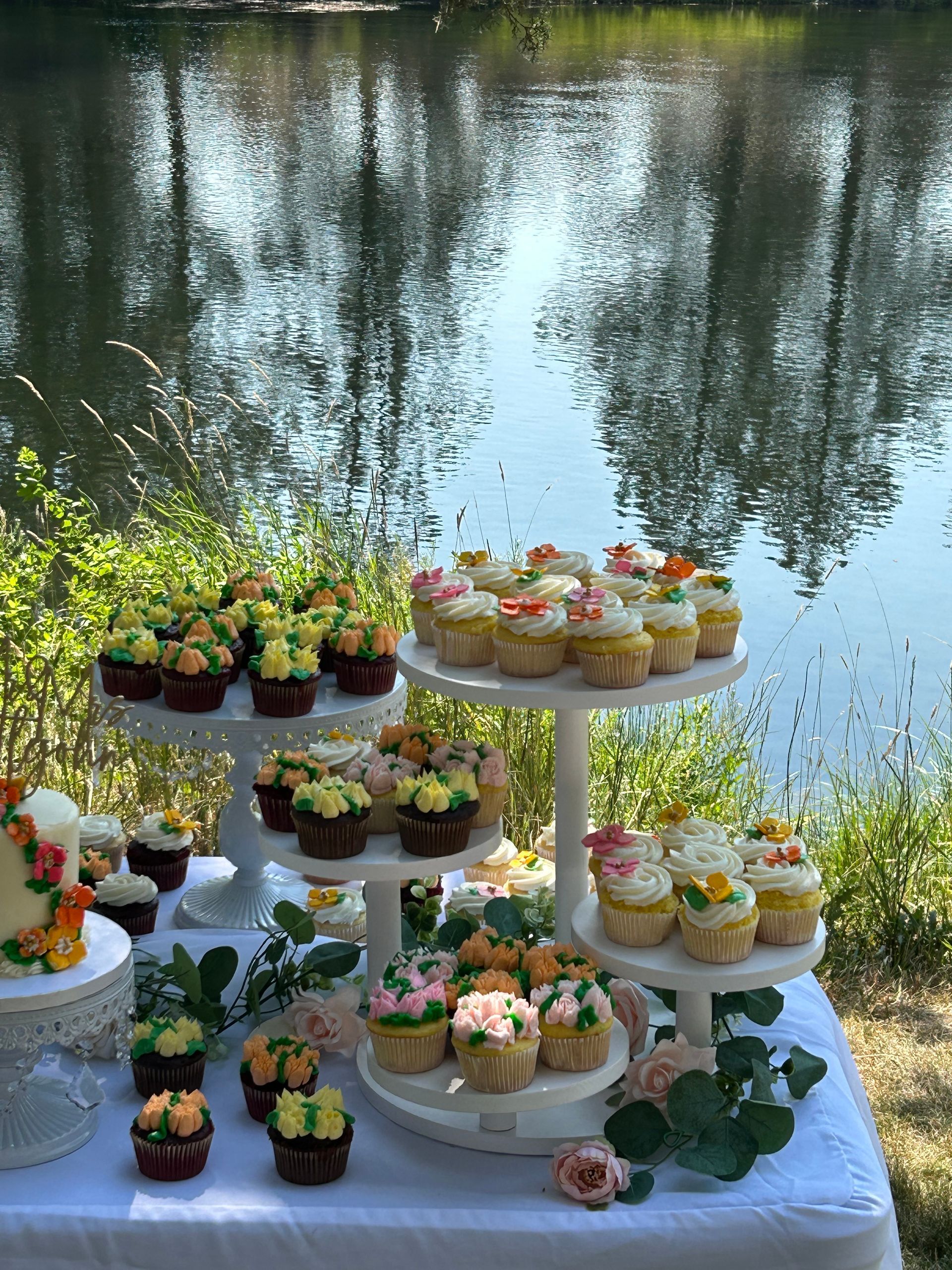 A table topped with cupcakes and a cake with a lake in the background.