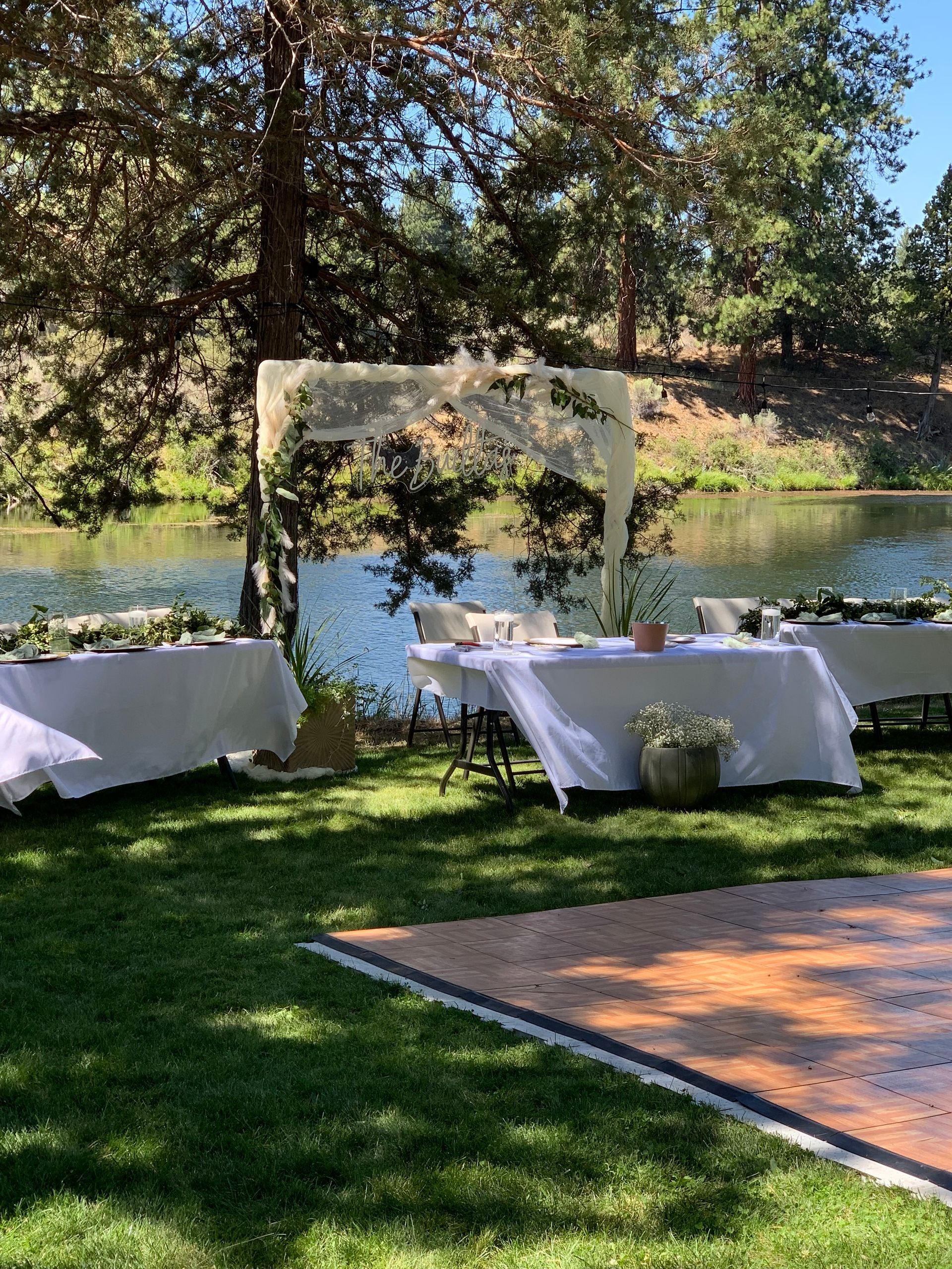 A wooden dance floor is in the middle of a lush green field next to a lake.