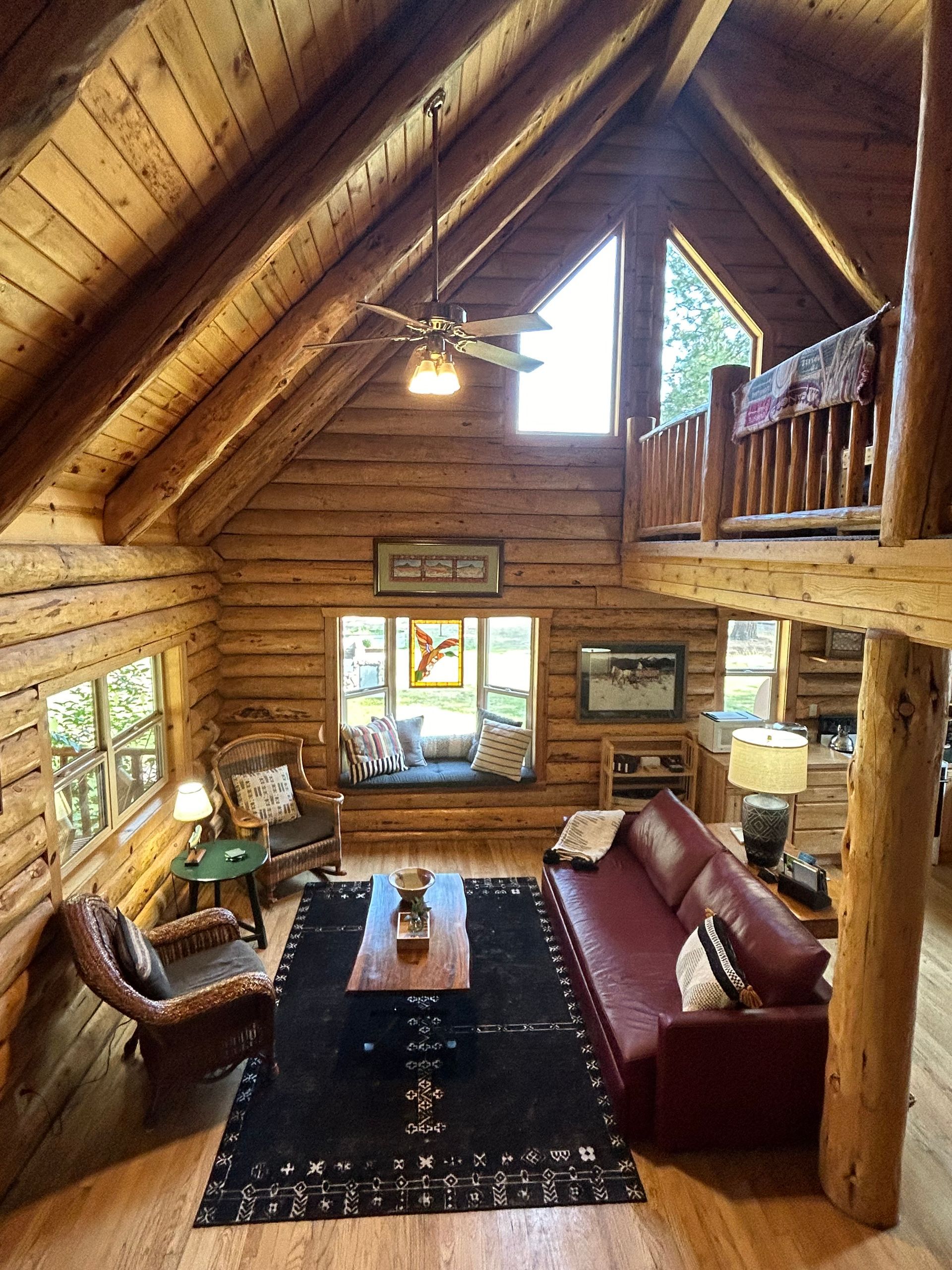 A living room in a log cabin with a couch , chairs , and a ceiling fan.