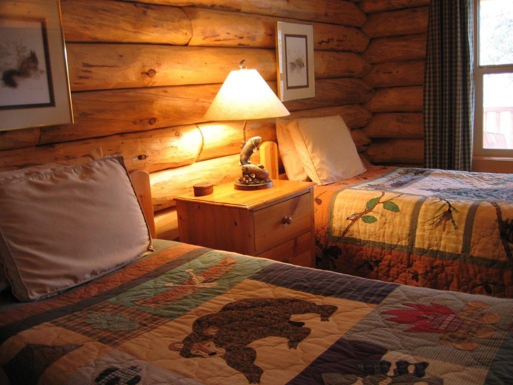 A bedroom in a log cabin with two beds and a lamp