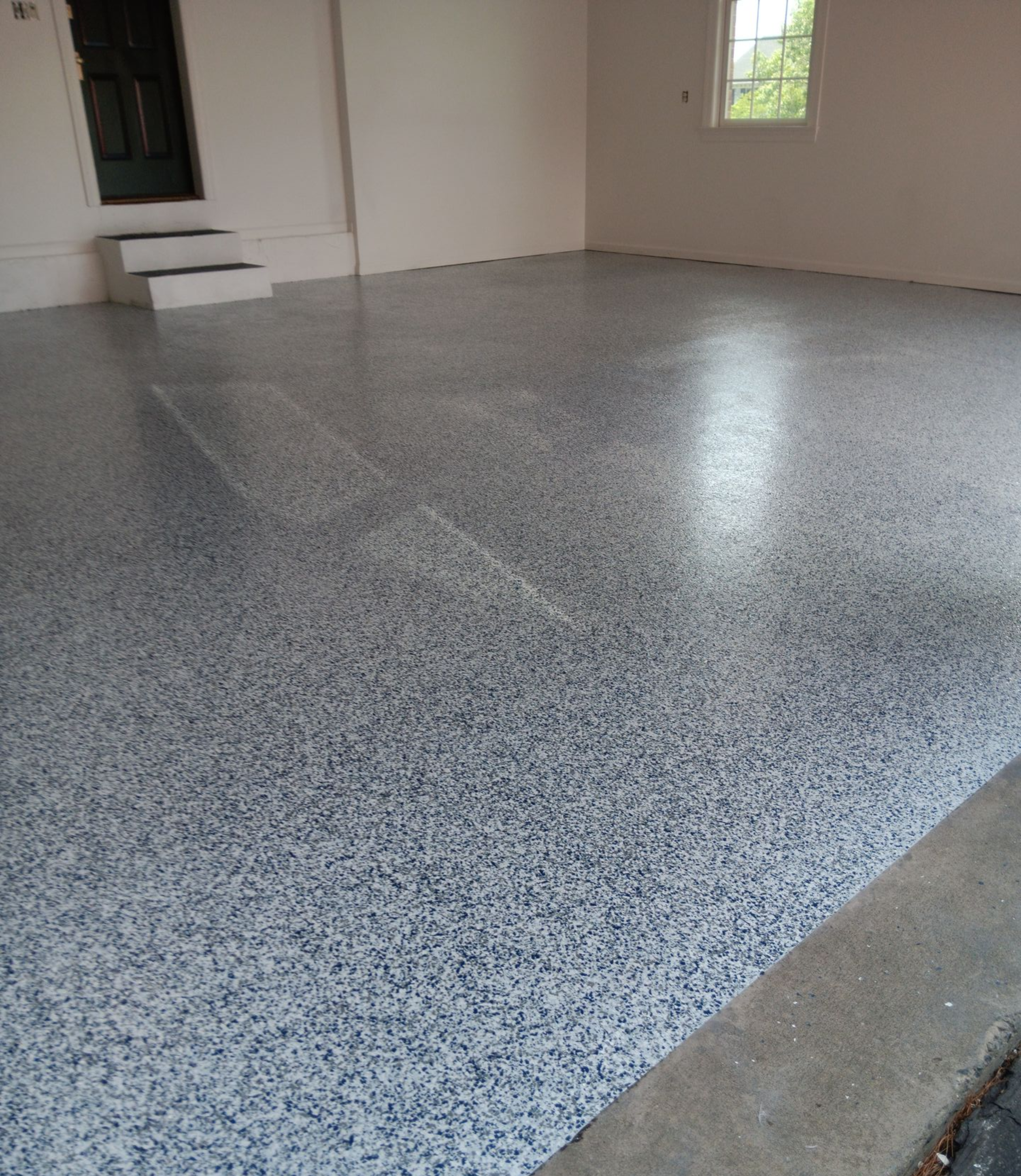 A room under construction with a grey speckled flake epoxy floor, purple drywall, and exposed plumbing pipes.