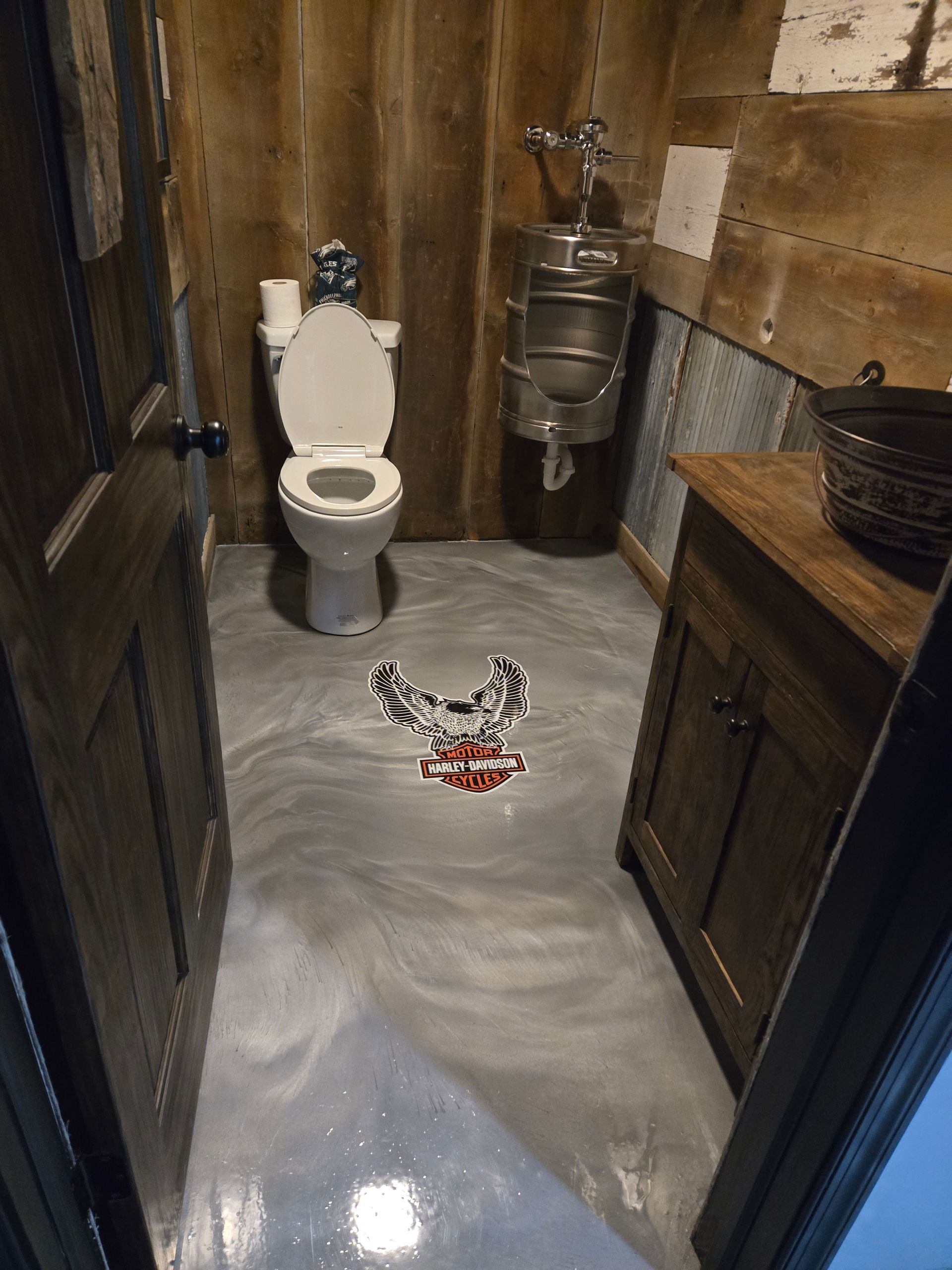 Rustic bathroom with gray epoxy floor, wood walls, toilet, and vintage metal sink.