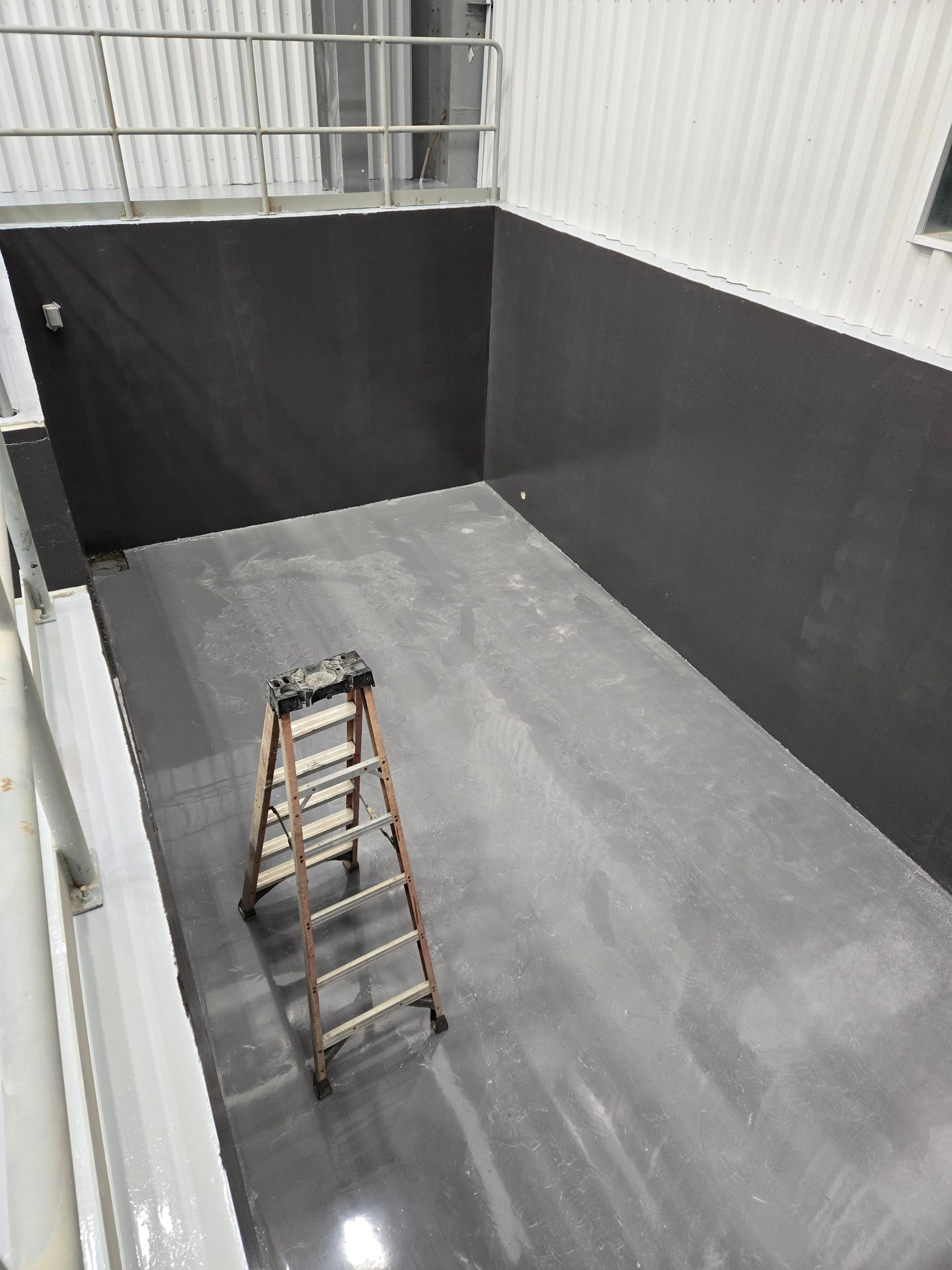 Interior of a gray-walled industrial space with a ladder. A metal railing is visible at the top.