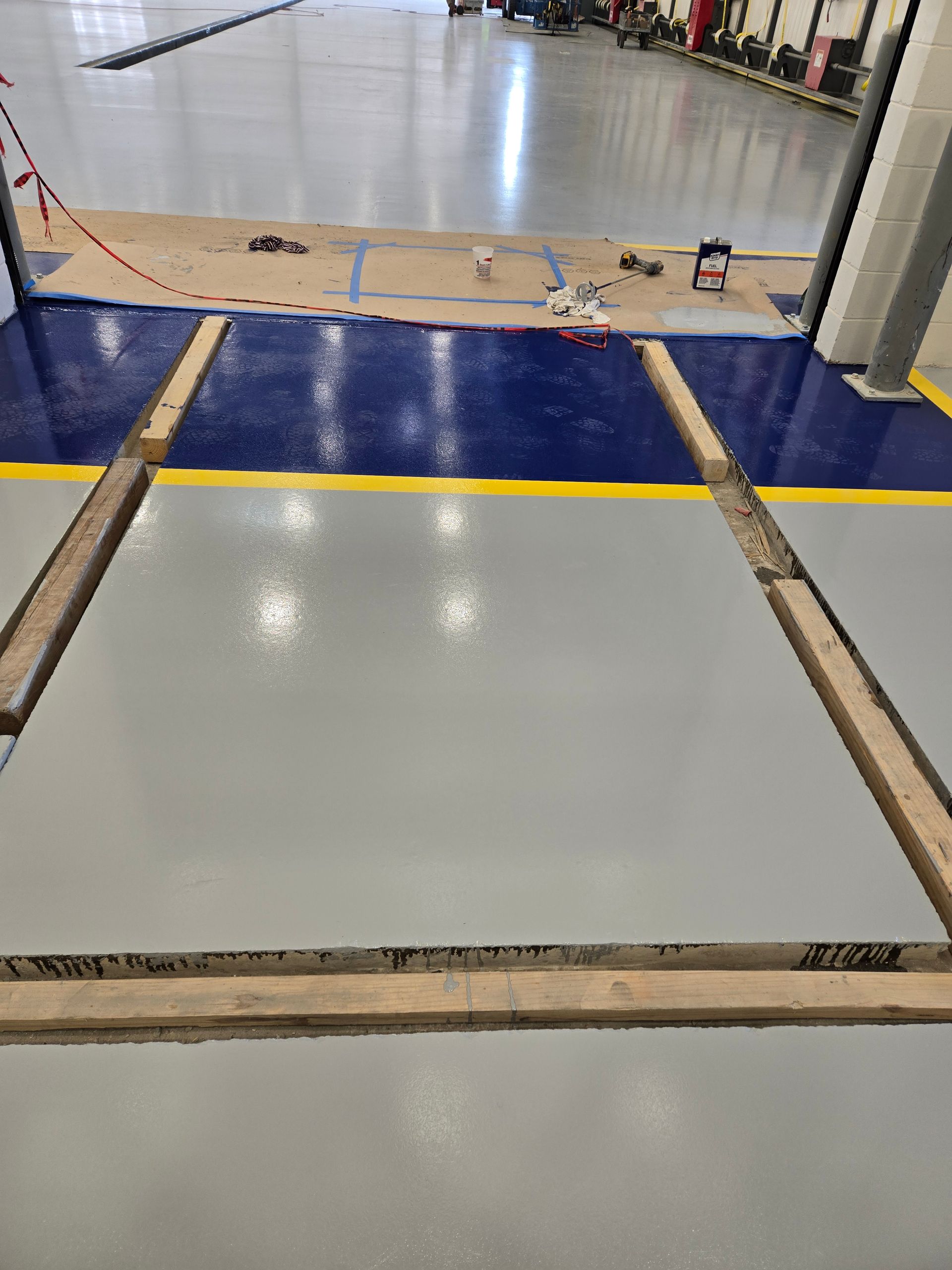 Newly painted gray floor inside a building, framed by wooden planks. Blue and yellow painted areas are in the background.