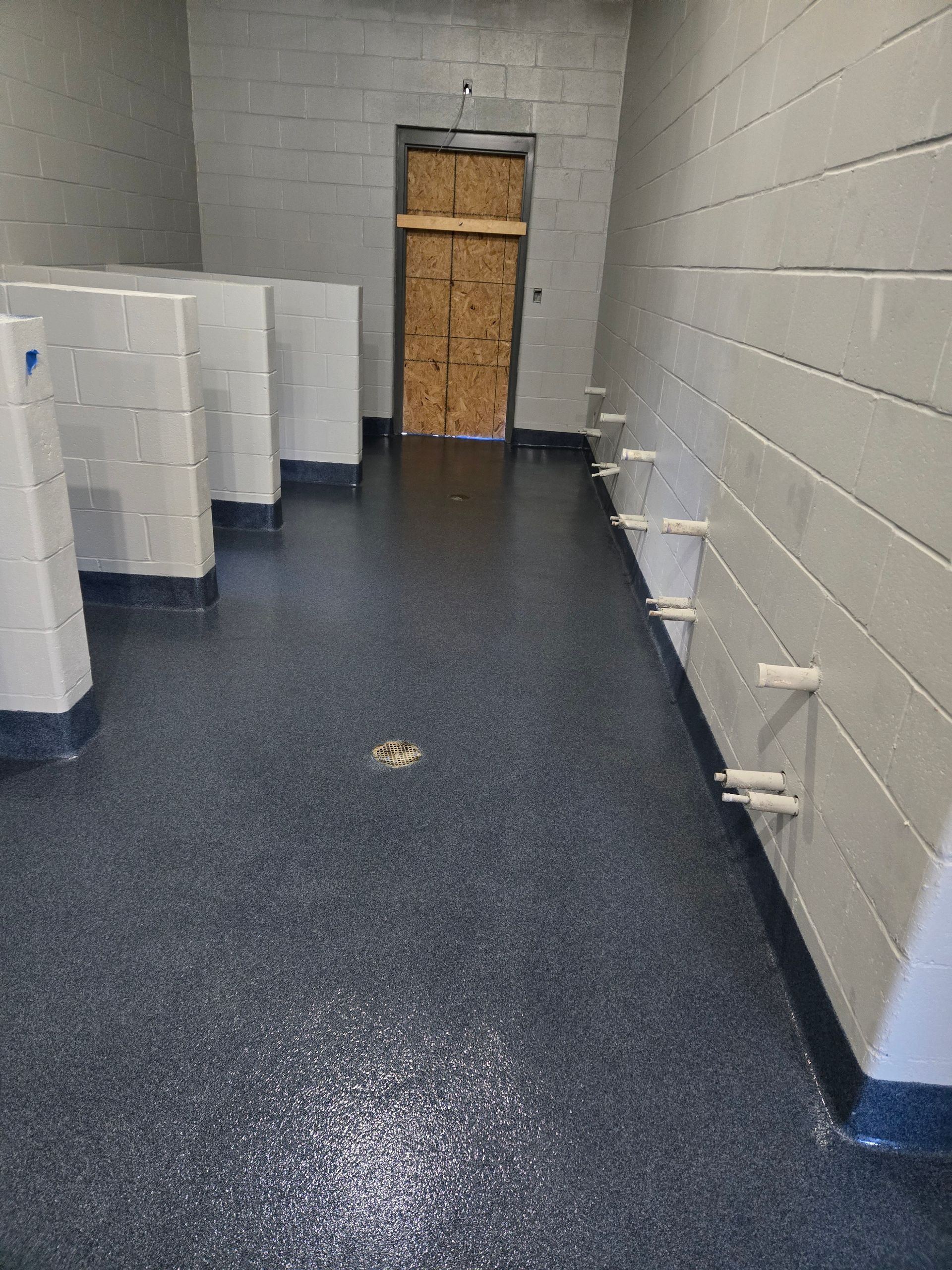 A public restroom with a dark speckled floor and cinder block walls; a boarded-up doorway is visible.