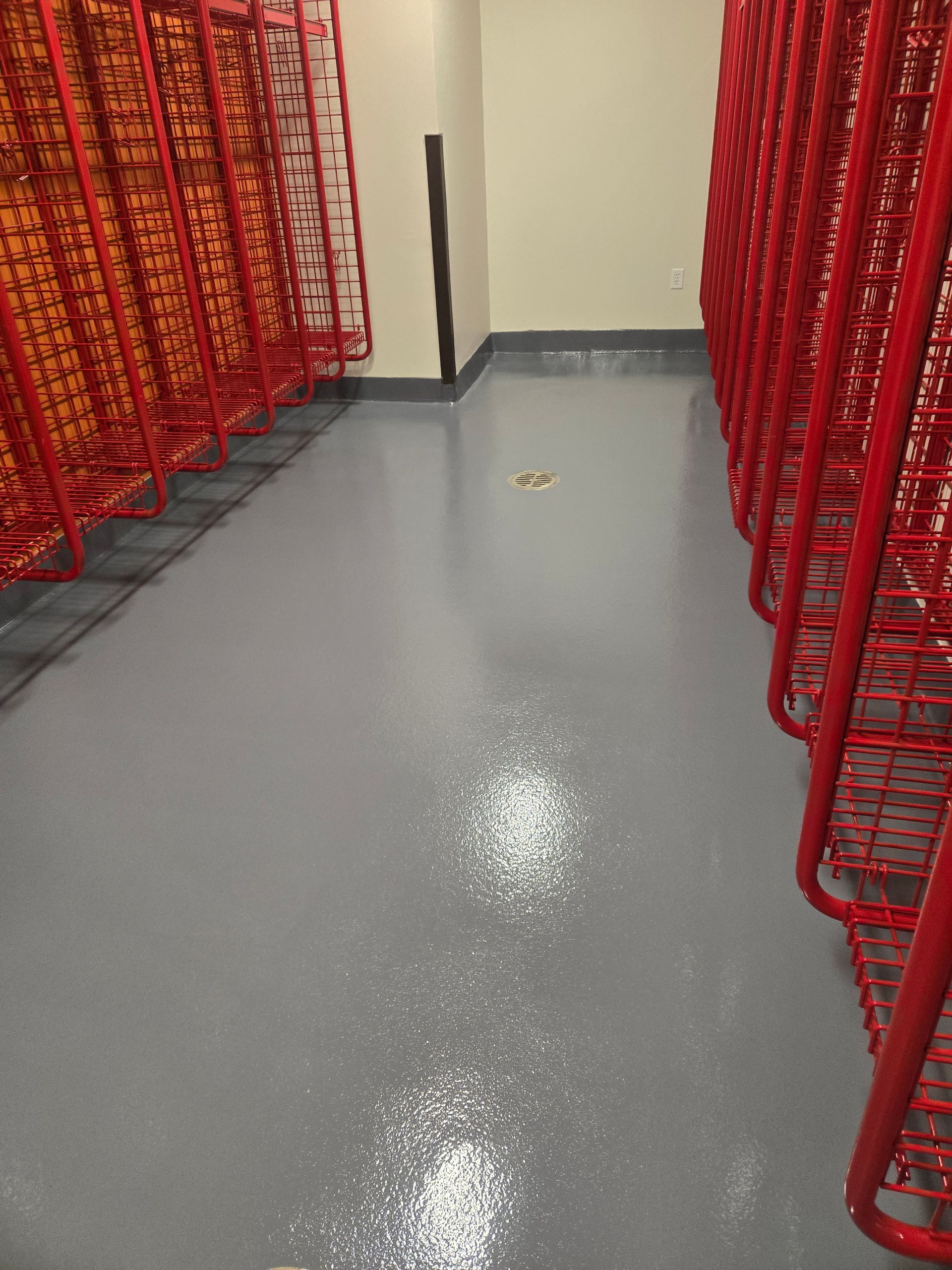 Gray floor in a storage room with rows of red metal racks on either side. A door is at the end.