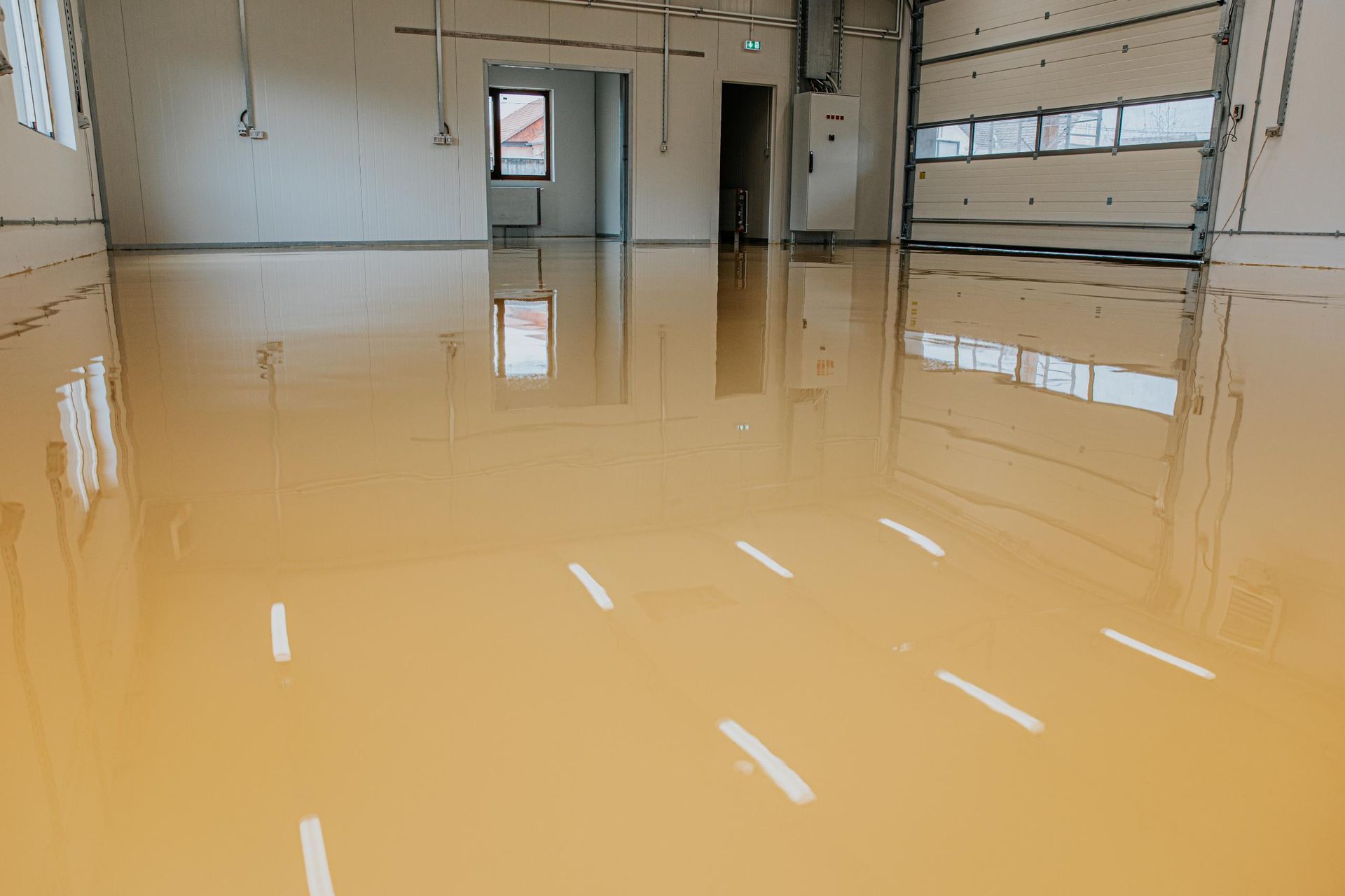 Shiny tan epoxy floor in a mostly empty room with a garage door and windows.