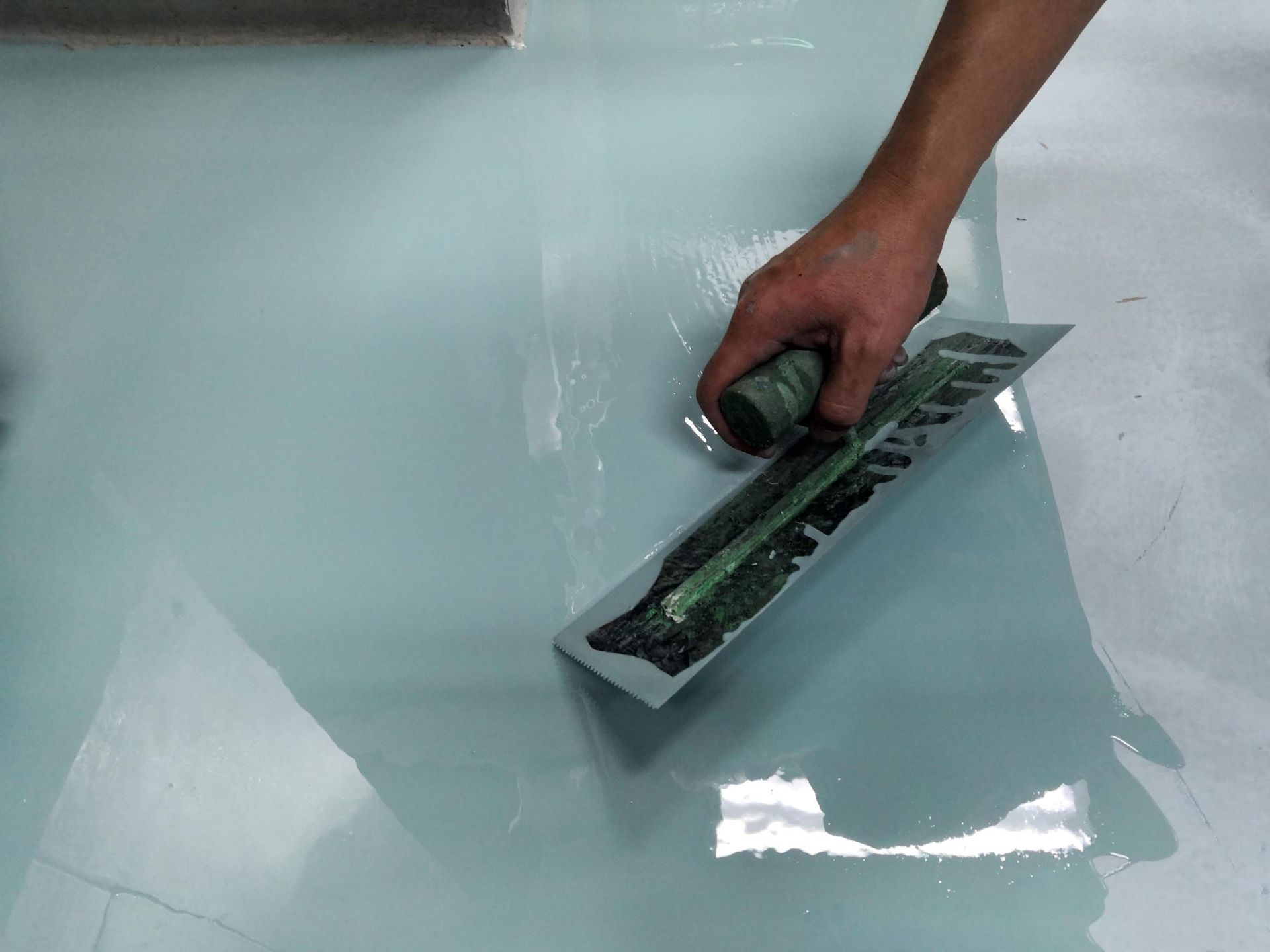 Person using a trowel to smooth light blue epoxy on a floor.