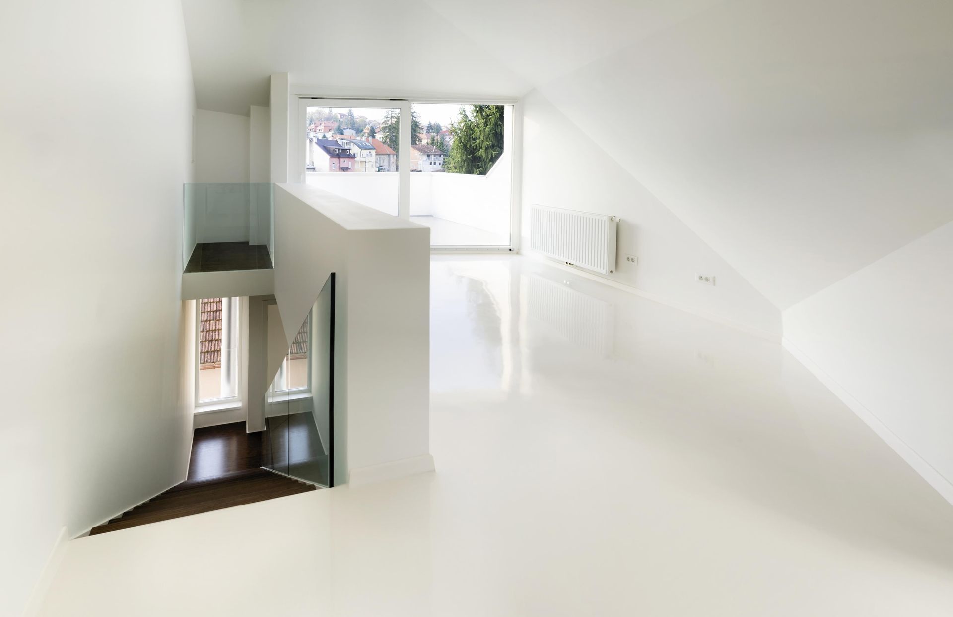 Bright white interior with sloped ceiling, windows, staircase, and glossy floor.