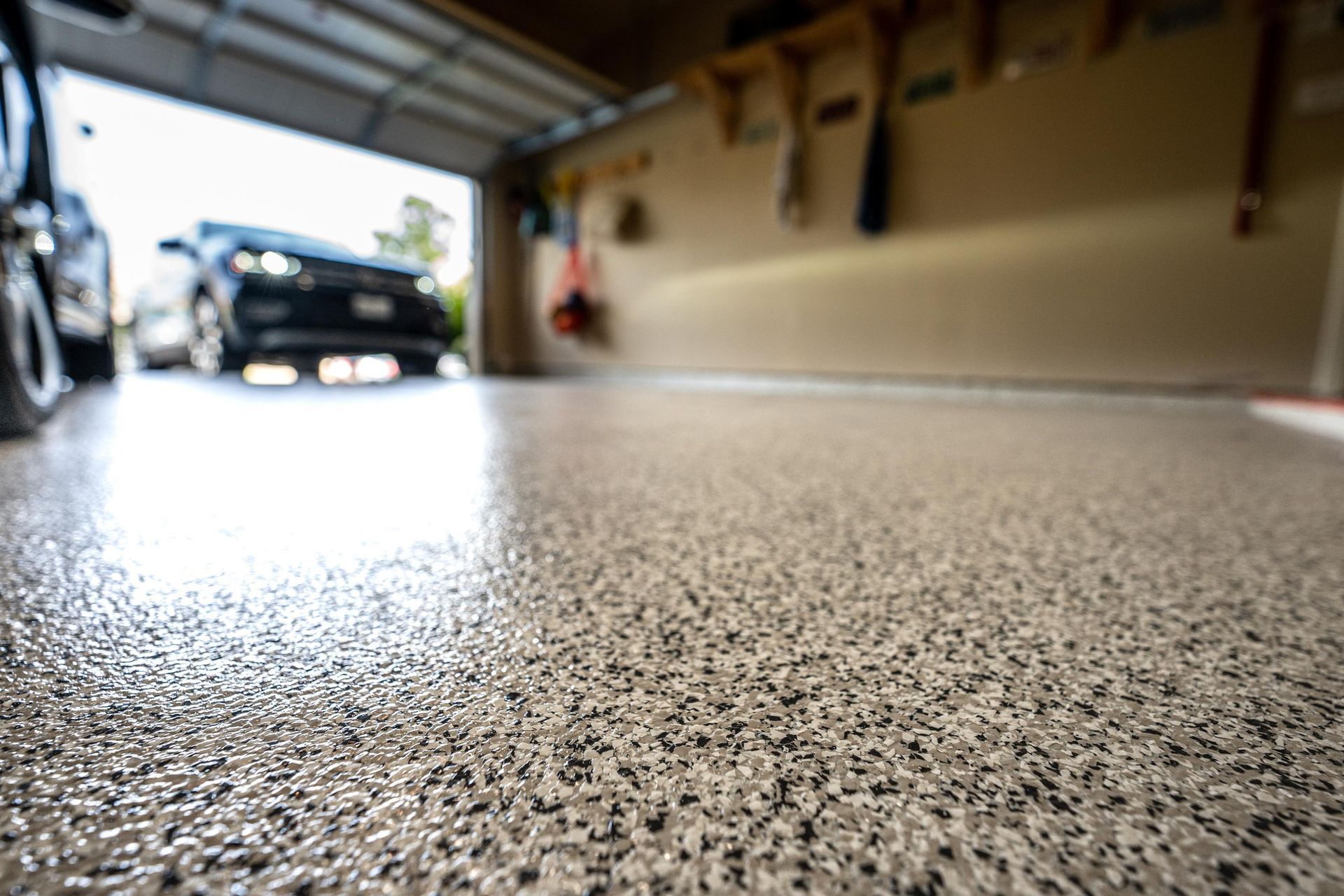 Close-up of a speckled, glossy garage floor with a car visible inside and the garage door open.
