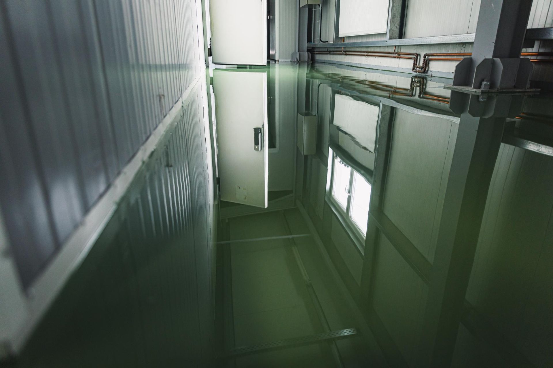 Green-floored industrial room reflecting walls and a window, door ajar.