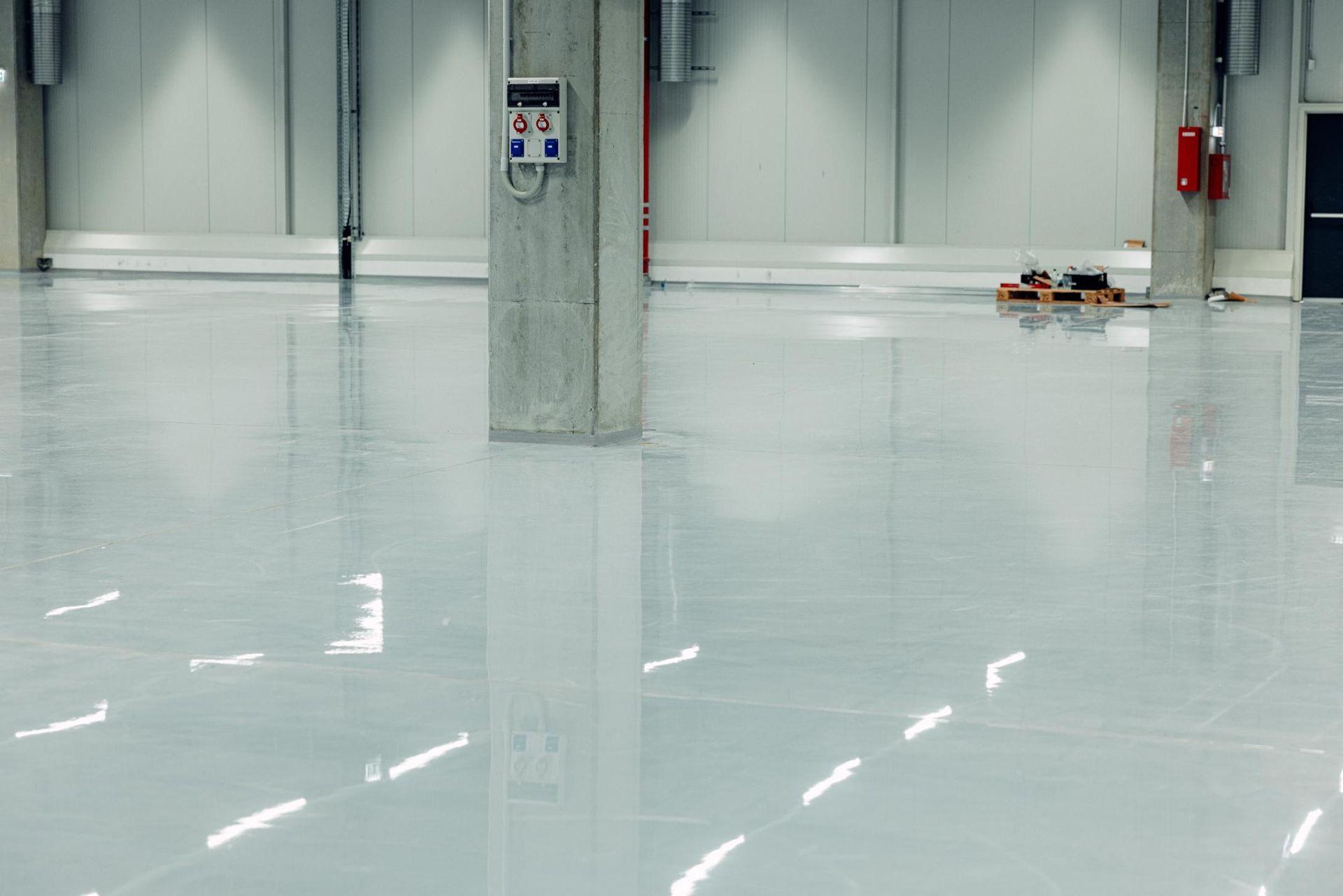 A spacious, minimalist warehouse with a glossy white epoxy floor reflecting overhead lights and a concrete support column.