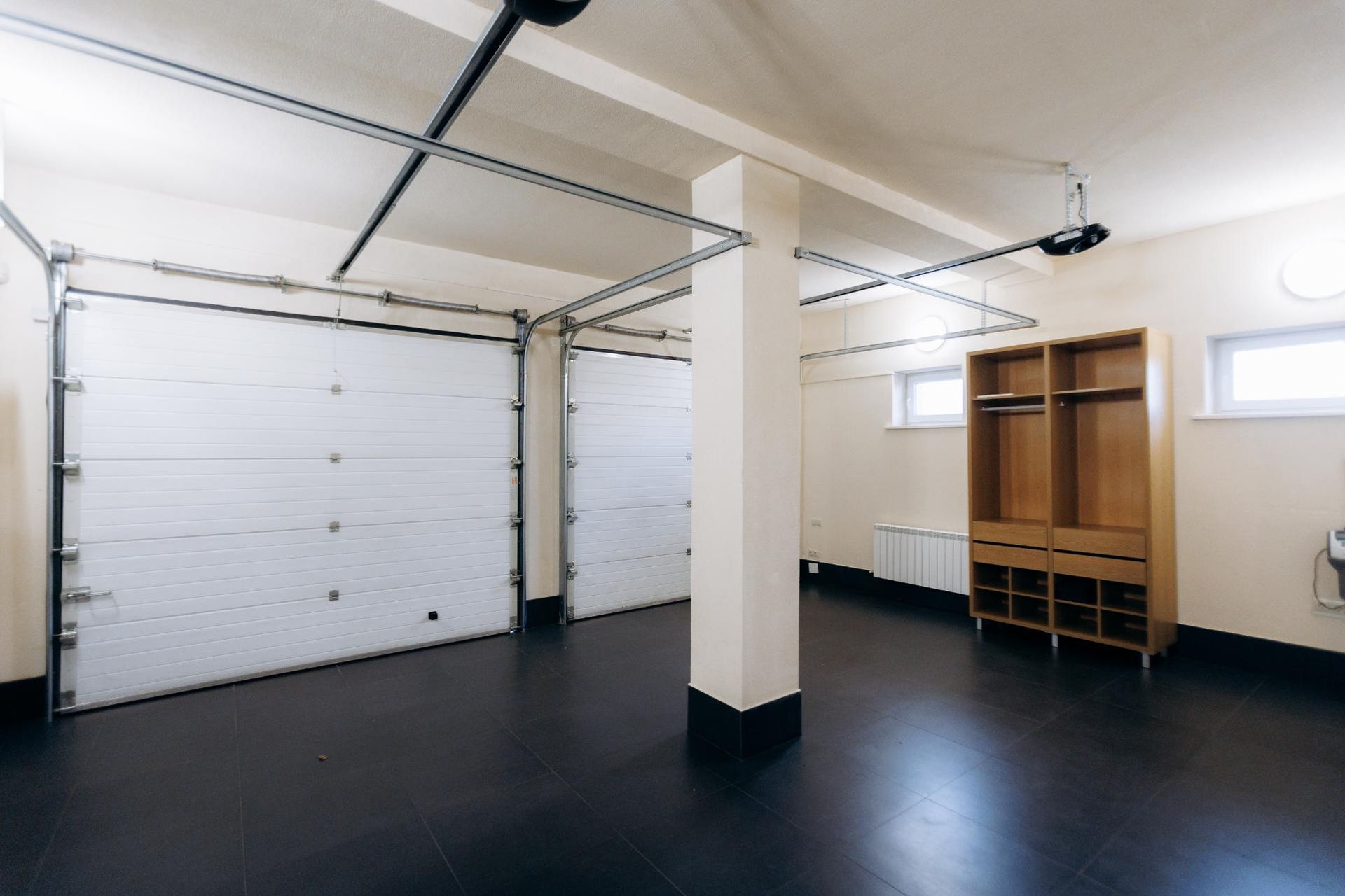 A bright garage with white doors, black floor, and a wooden storage unit.