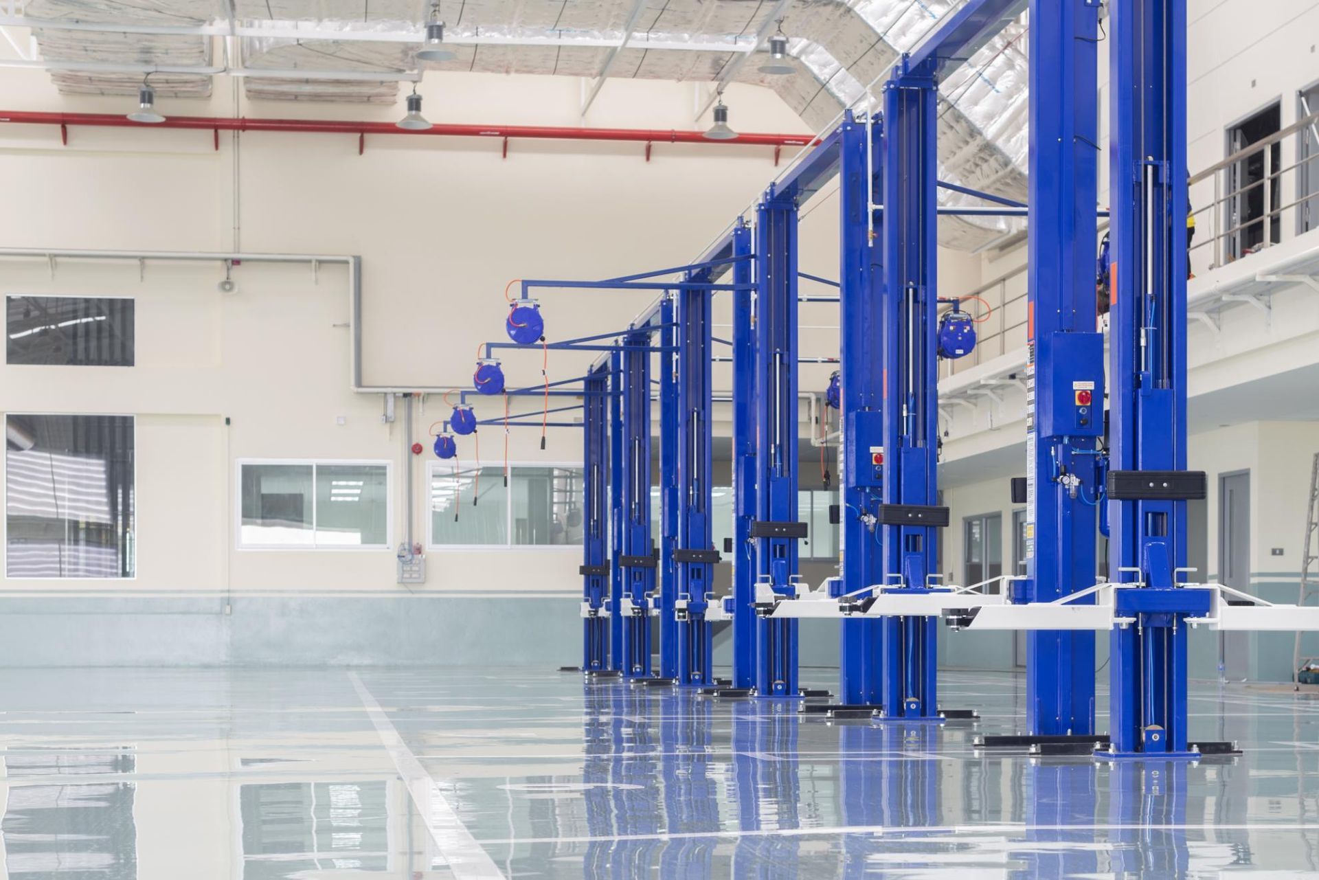 Row of blue car lifts in a bright, empty garage with a shiny floor.