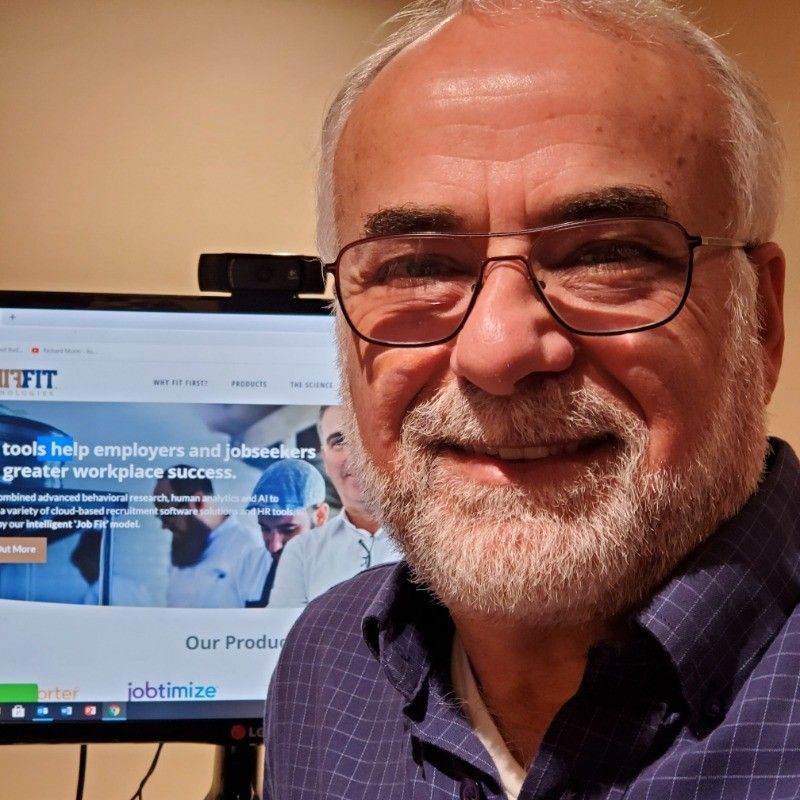 Man wearing glasses smiles in front of a computer displaying a website.