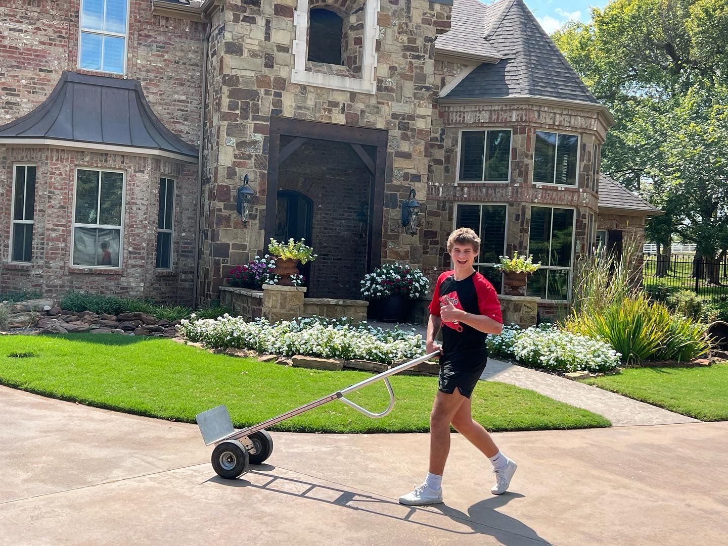 A person walks on a driveway in front of a stone house while pulling a two-wheeled measuring tool.