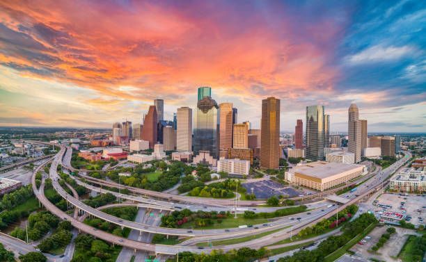 Aerial view of the Houston, Texas skyline at sunset with a vibrant orange and blue sky over city skyscrapers and highways.