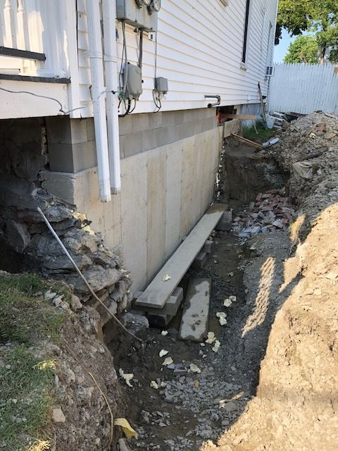 The side of a house is being remodeled and there is a hole in the ground.