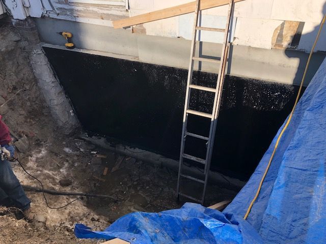 A man is digging a hole in the ground next to a ladder and a blue tarp.