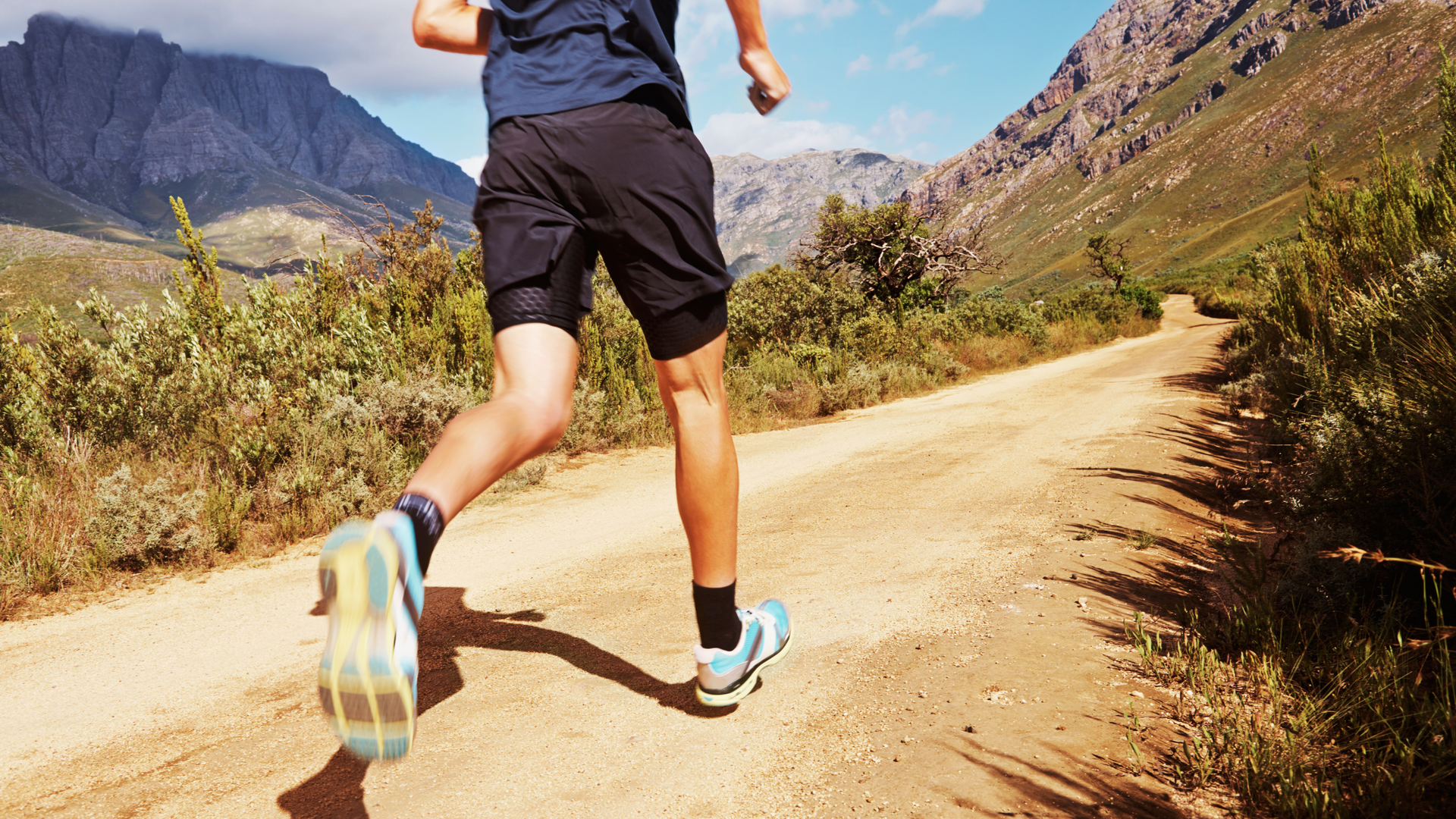 A man is running down a dirt road in the mountains.