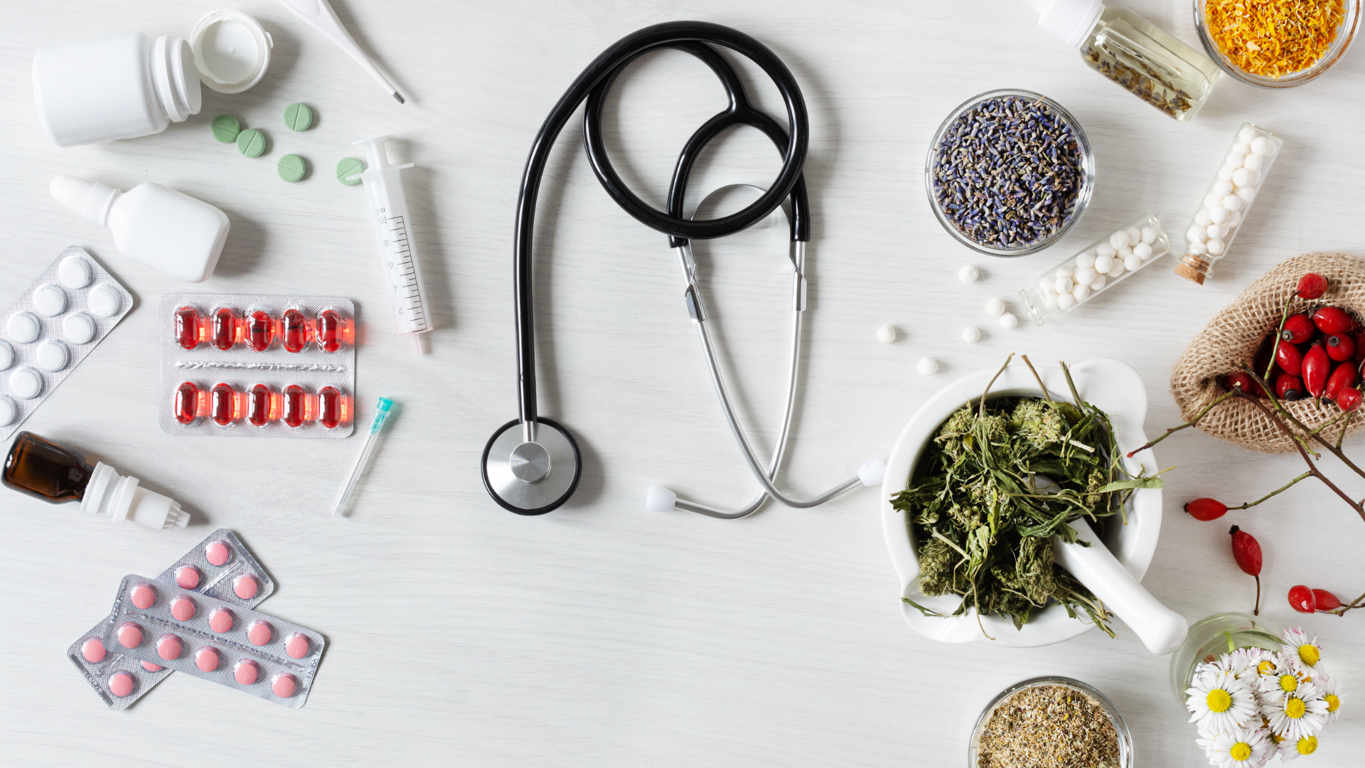 A stethoscope , mortar and pestle , pills , and herbs are on a table.