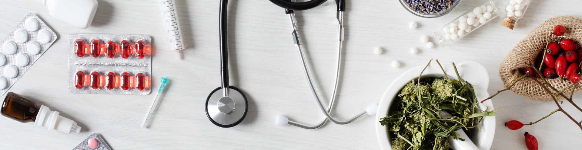 A table topped with a stethoscope , pills , a bowl of herbs and a bowl of berries.