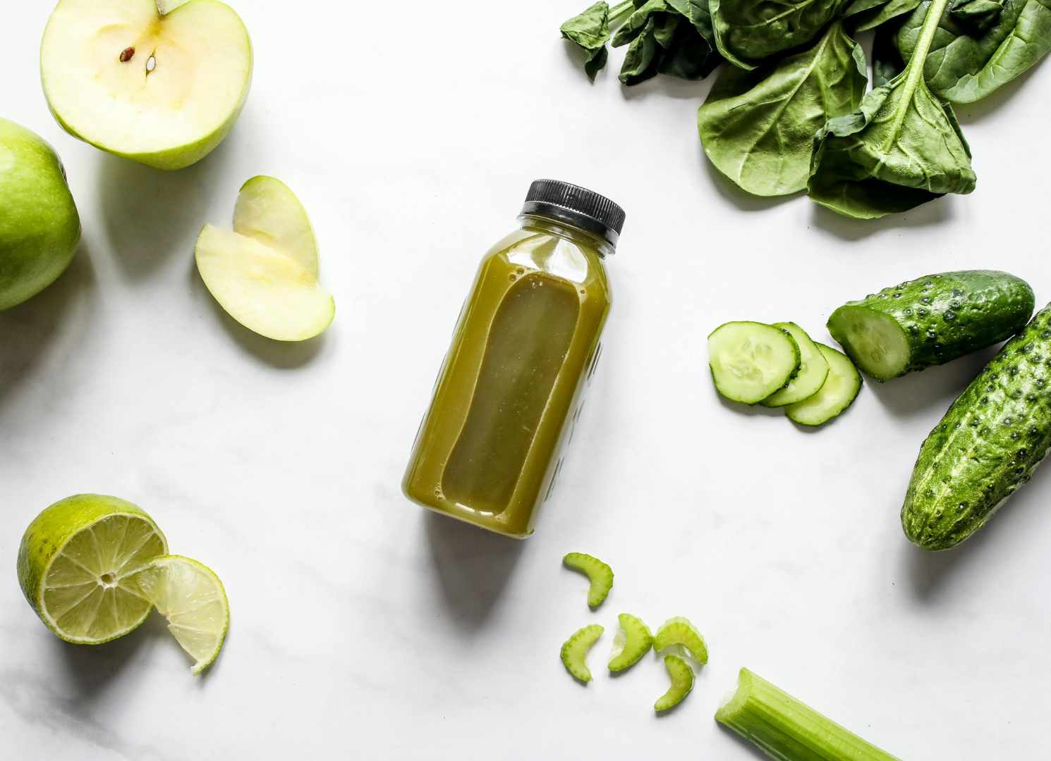 A bottle of green juice surrounded by fruits and vegetables on a table.