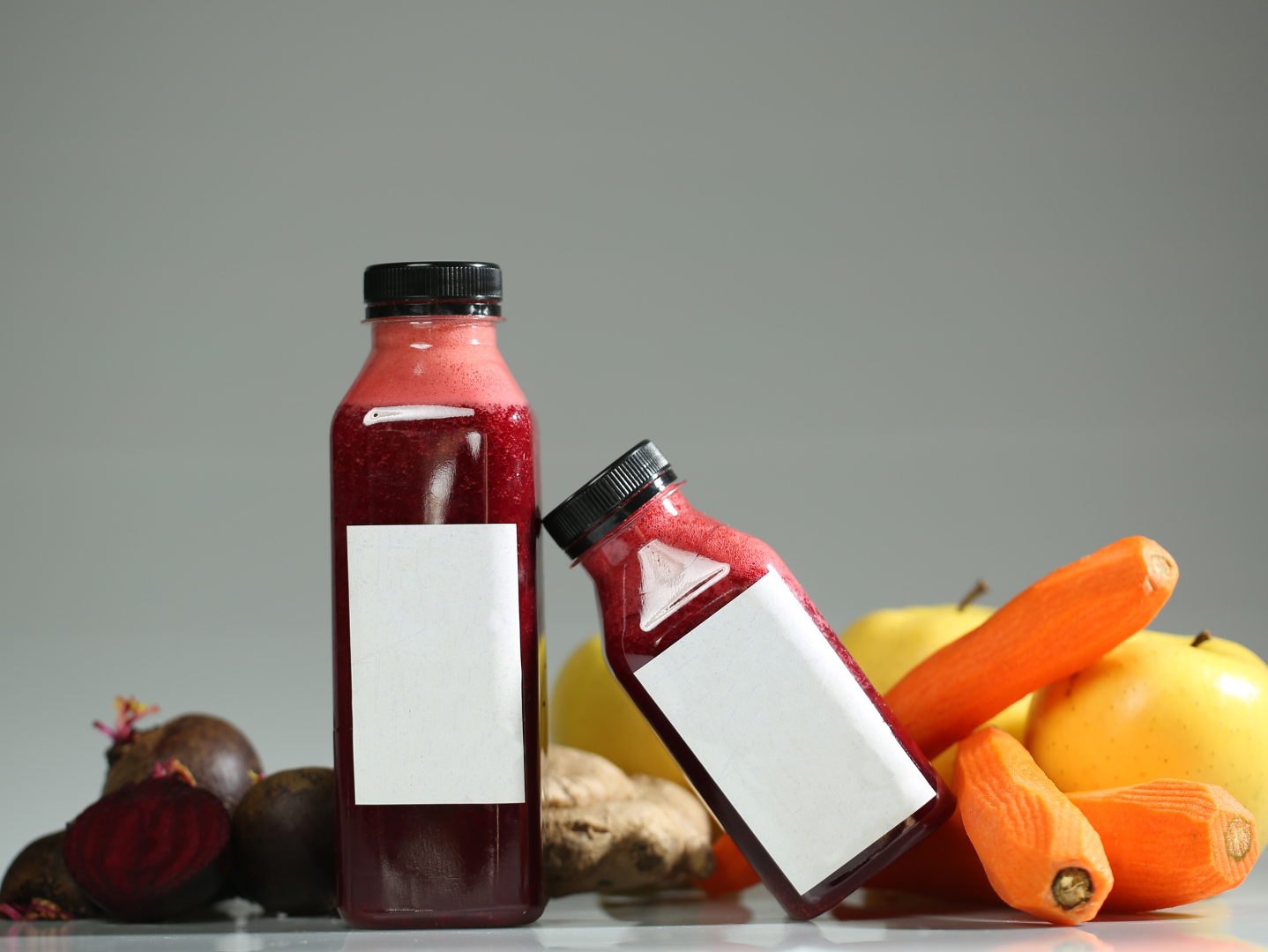 Two bottles of juice are sitting on a table next to fruits and vegetables.